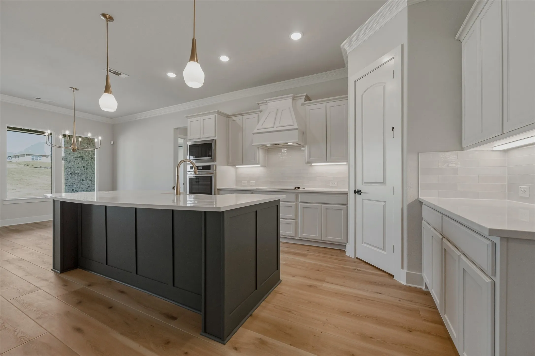 Kitchen featuring a dark grey center island with a light-toned countertop, white cabinetry with integrated appliances, light wood-finish flooring, and pendant lighting
