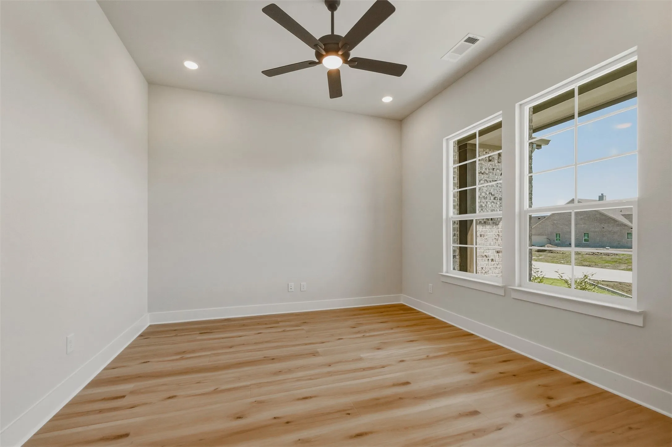 Wood-finish flooring, recessed lighting, ceiling fan, and two large windows with white trim