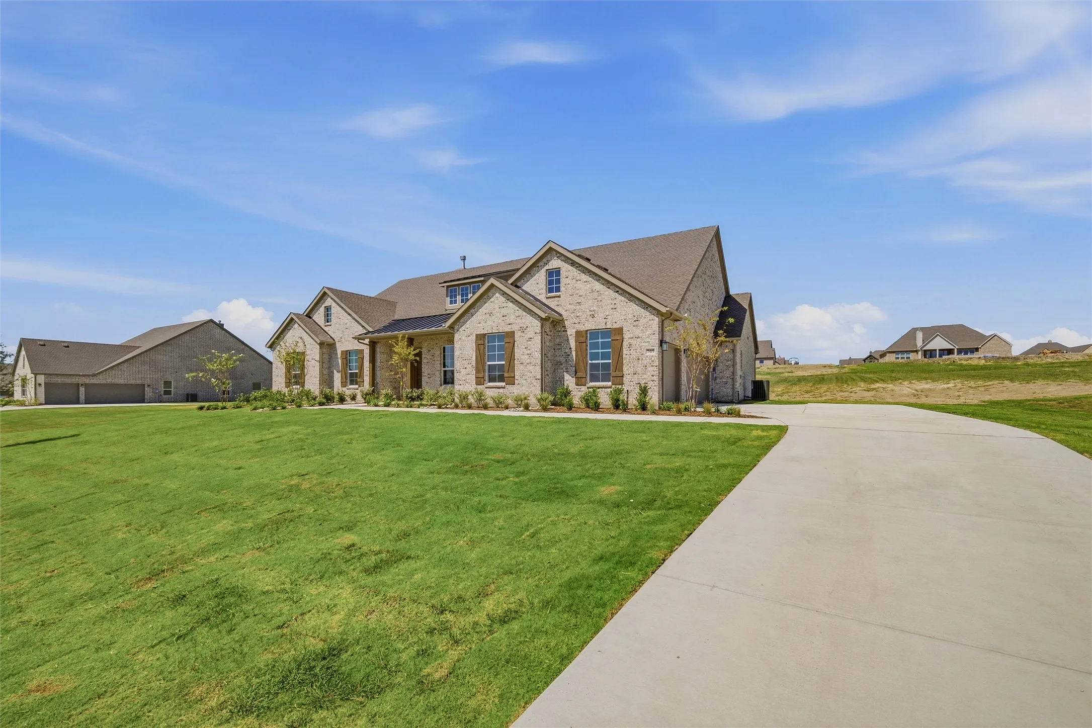 Brick exterior, dormer windows, attached garage, concrete driveway, and manicured lawn