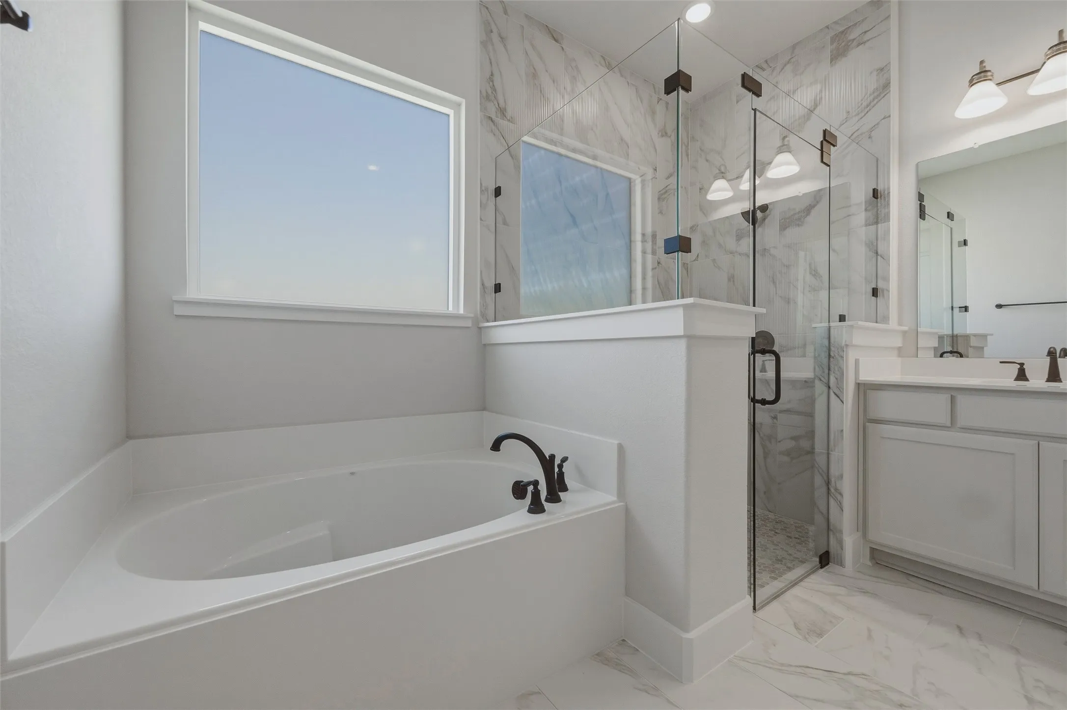Corner soaking tub with dark bronze fixtures, glass-enclosed shower with a marble-finish surround, dual vanity with white cabinetry and integrated sinks, and marble-finish flooring