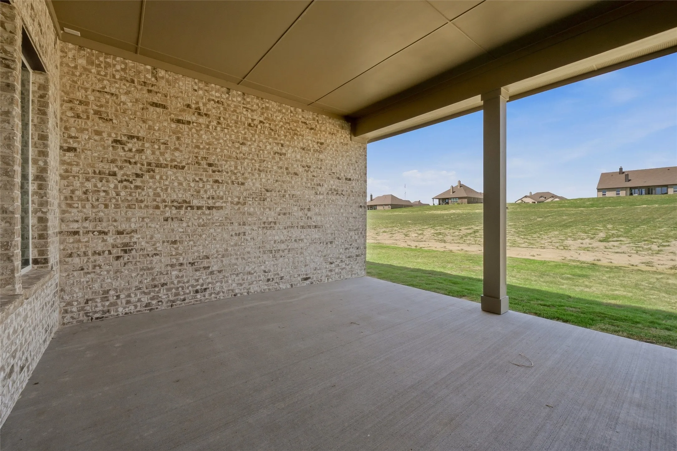 Covered patio with concrete flooring, brick exterior wall, and structural support columns