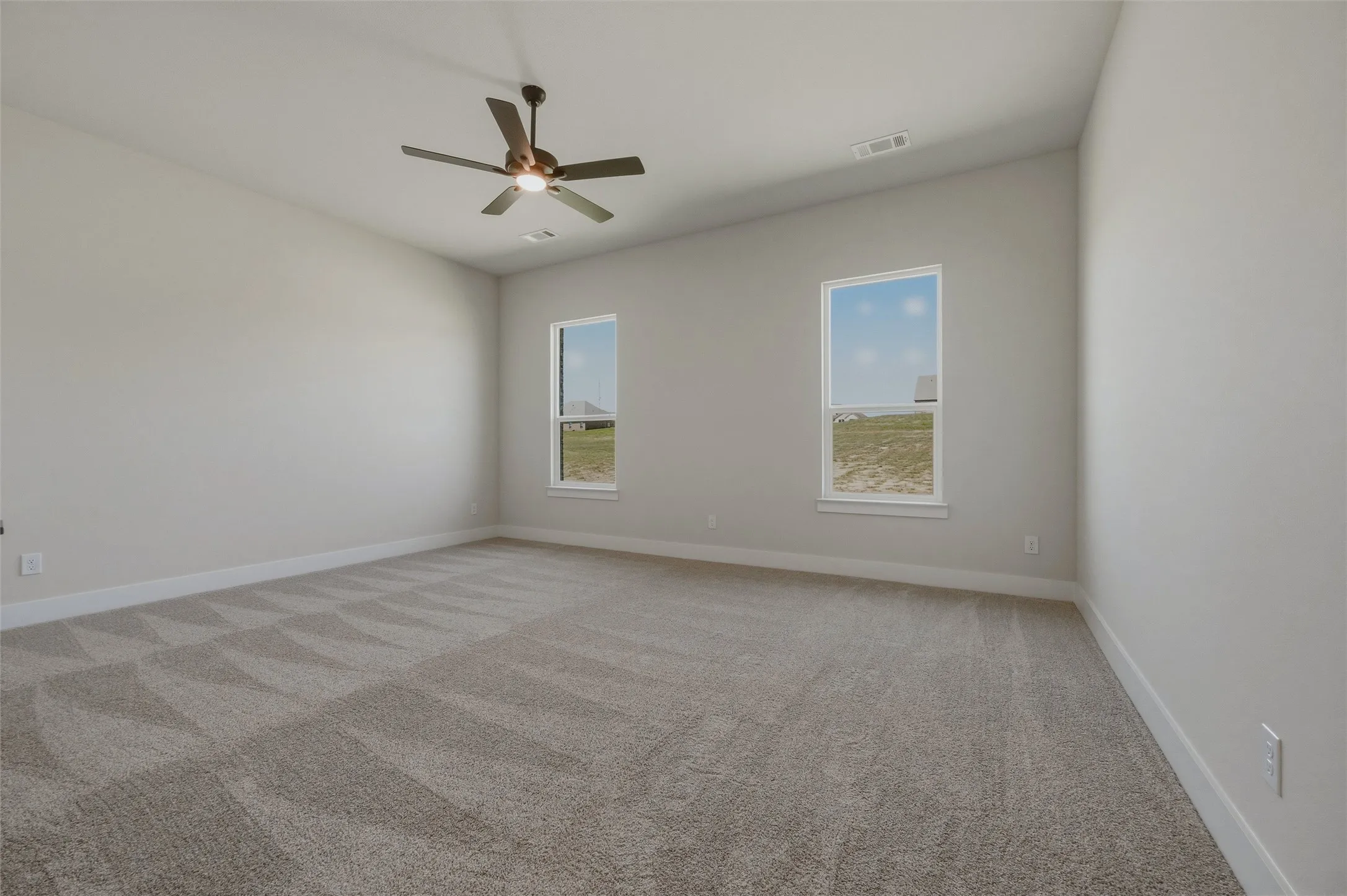 Carpeted interior space featuring two windows, a ceiling fan, and light-toned walls