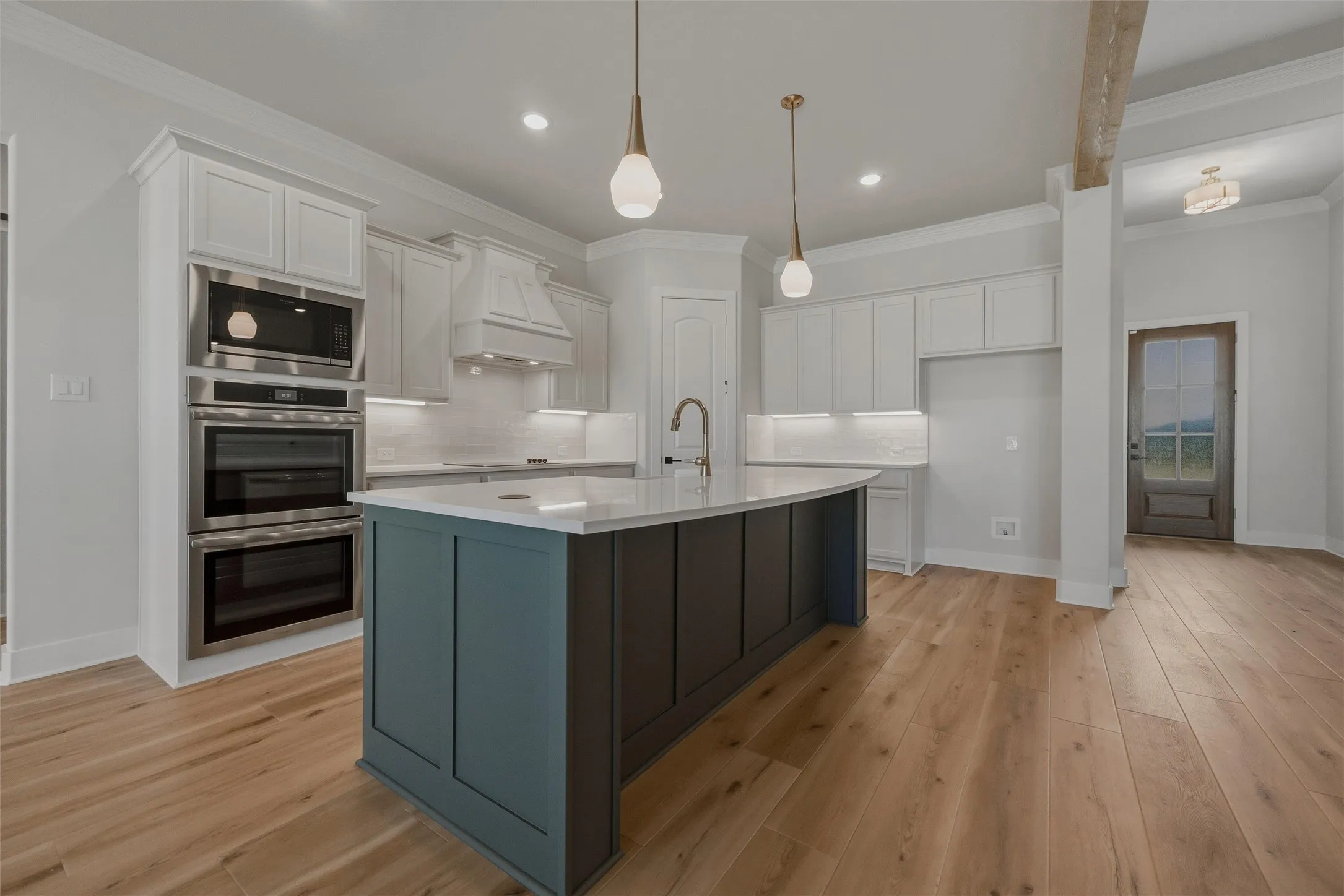 Kitchen featuring a curved island with contrasting paneling, stainless steel double wall ovens and microwave, under-cabinet lighting, and wood-finish flooring