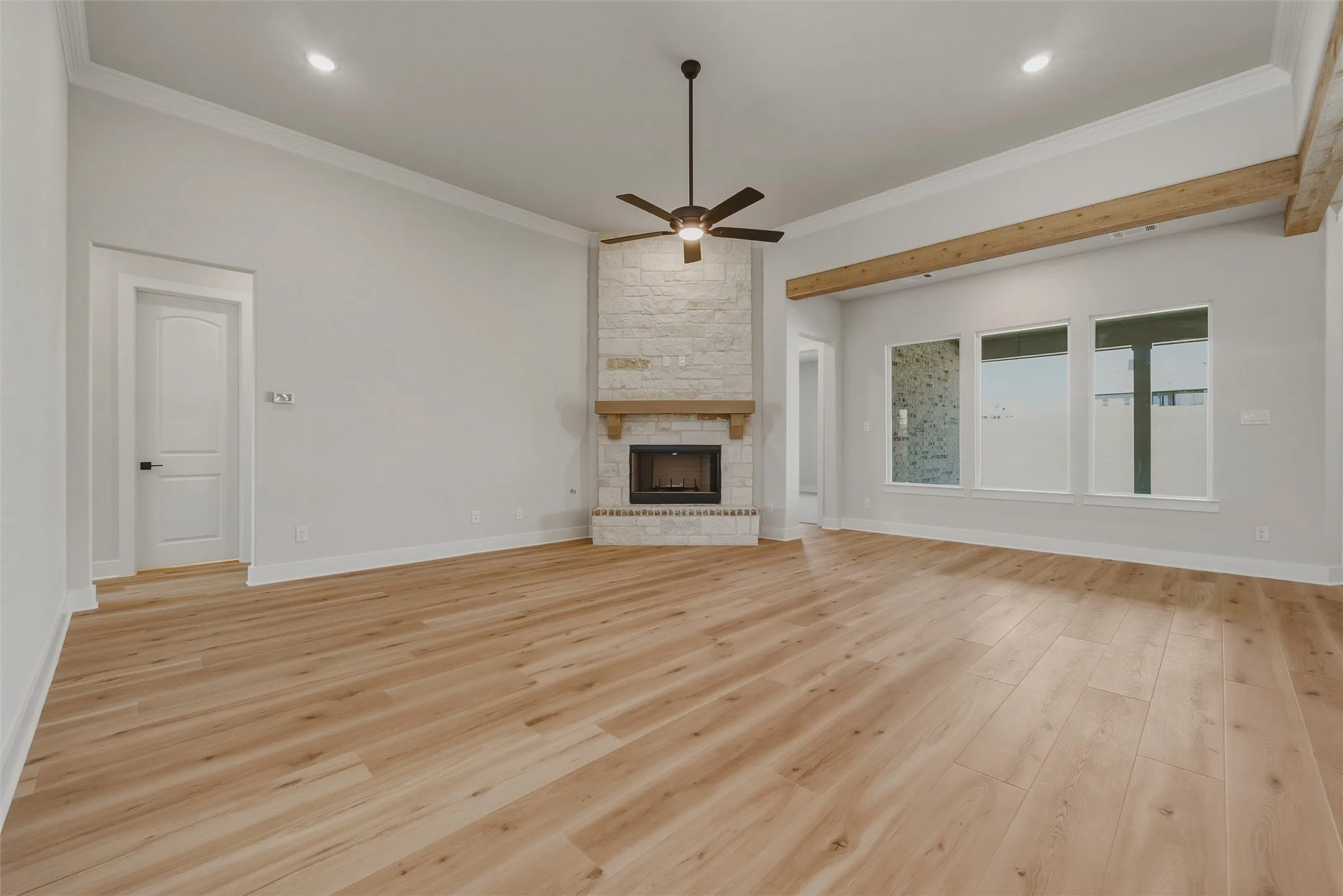Spacious room featuring wood-finish flooring, a stone fireplace with a wood mantle, a ceiling fan, recessed lighting, and multiple large windows