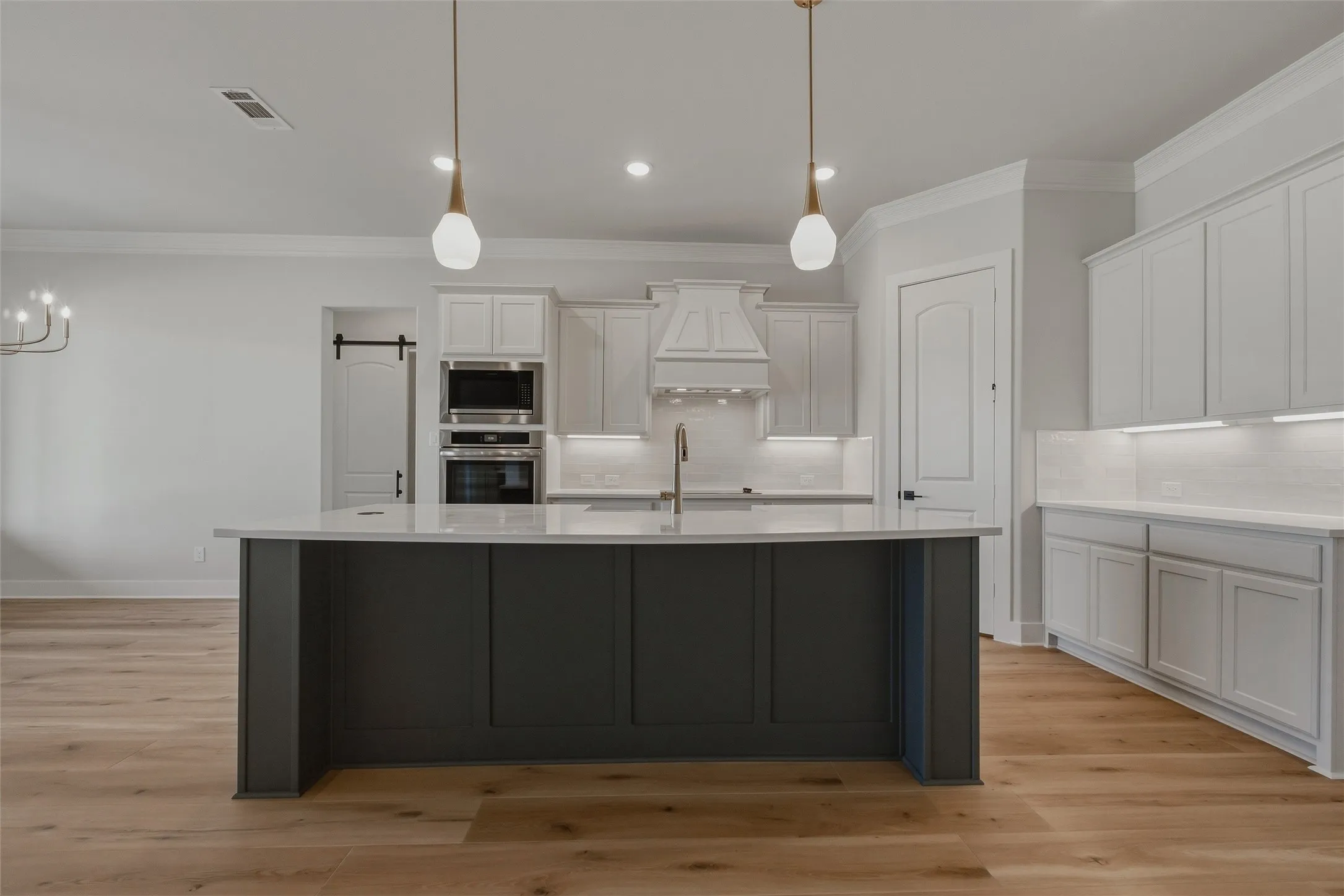 Modern kitchen featuring a large central island, white cabinetry, built-in appliances, and wood-finish flooring