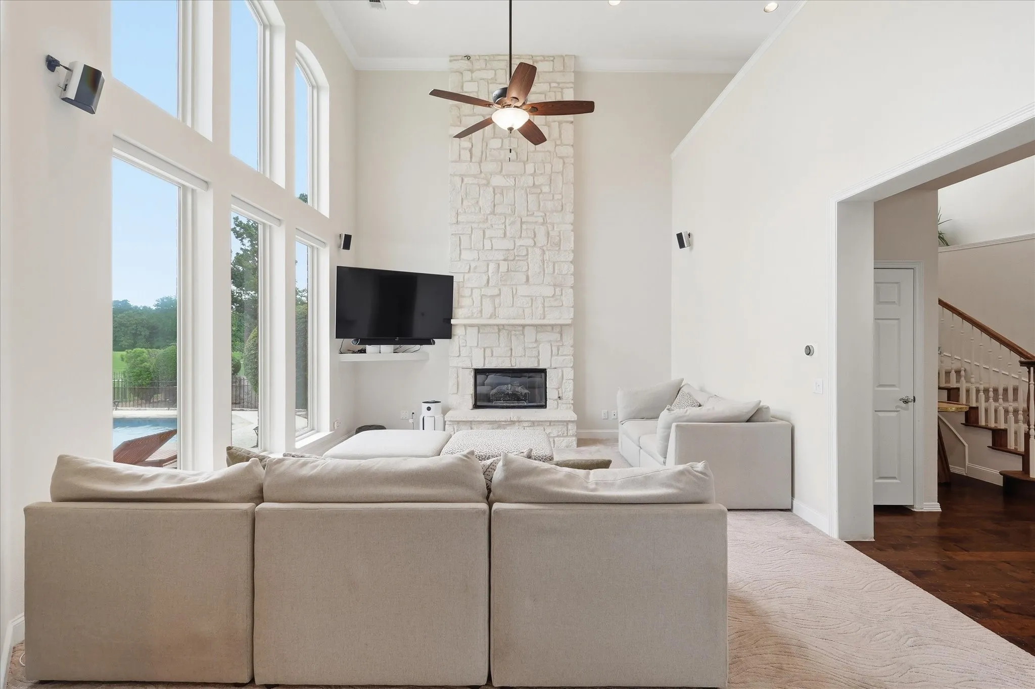 Spacious living area featuring a floor-to-ceiling stone fireplace, high ceilings, large multi-pane windows, a ceiling fan, and recessed lighting
