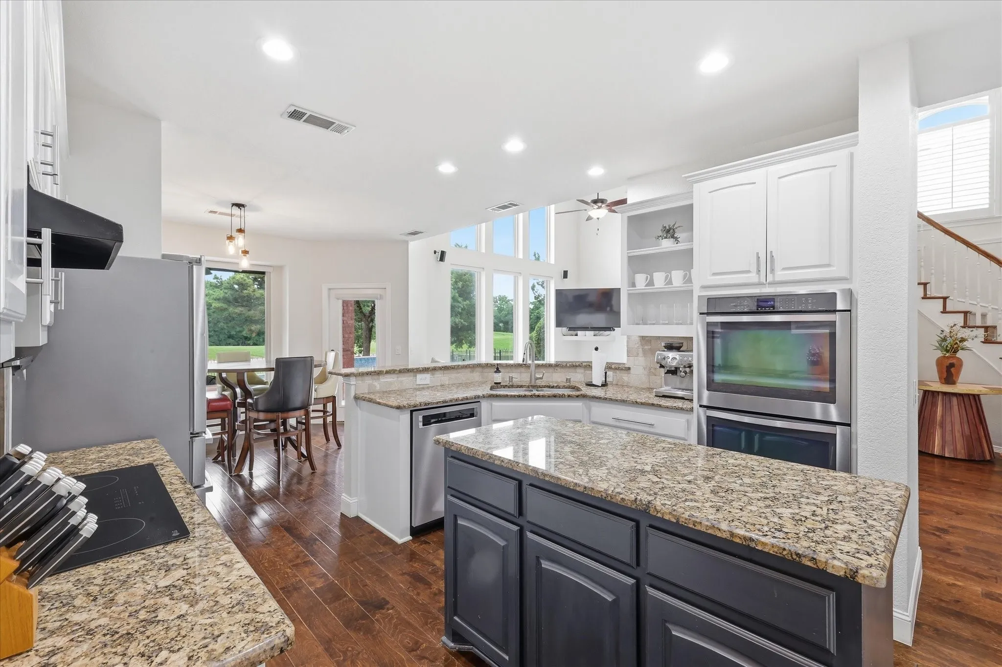 Kitchen featuring granite countertops, wood-finish flooring, white cabinetry, built-in double ovens, and an expansive island
