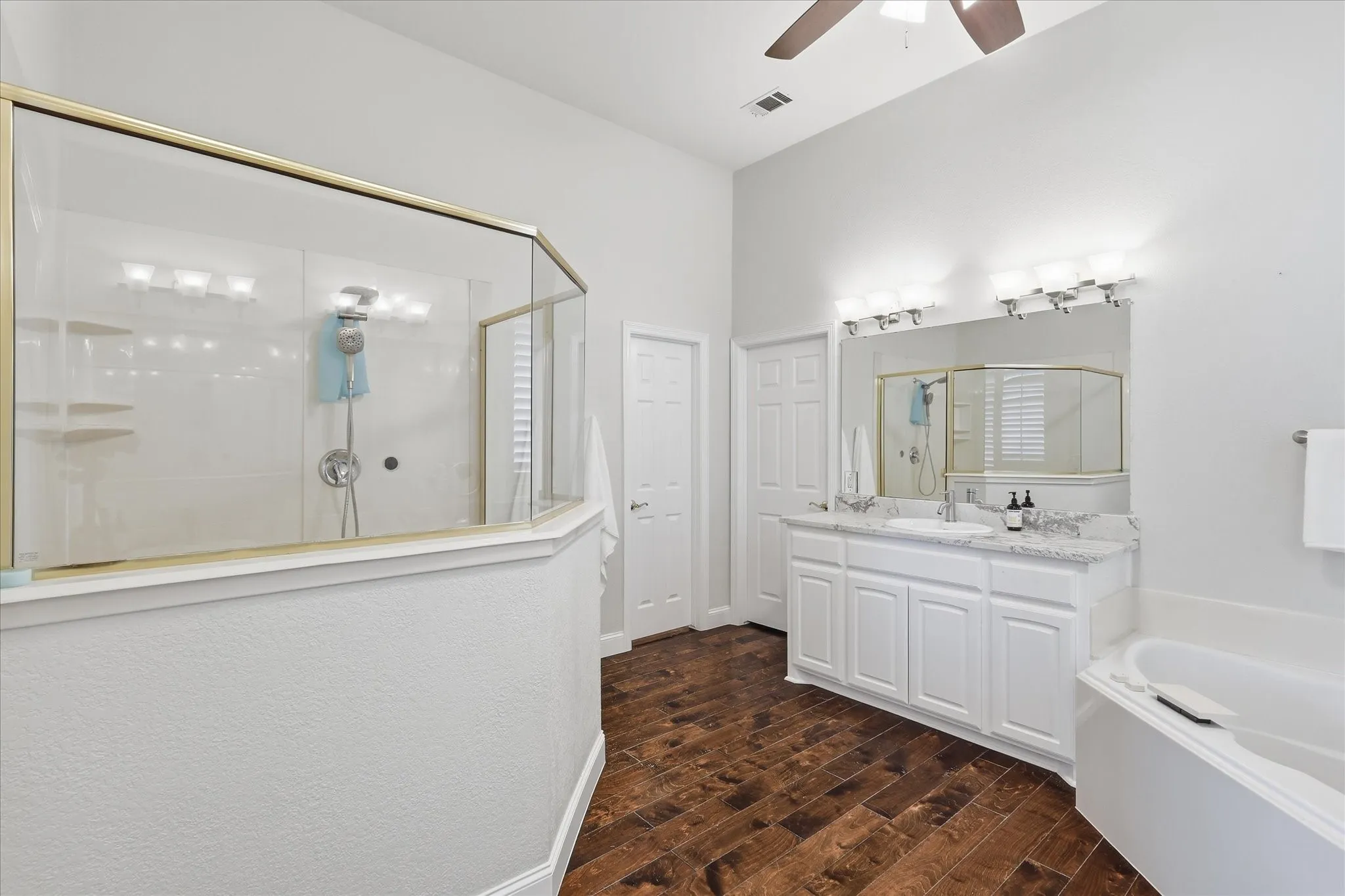 Spacious bathroom featuring a glass-enclosed shower, dual vanity with undermount sinks, and wood-finish flooring