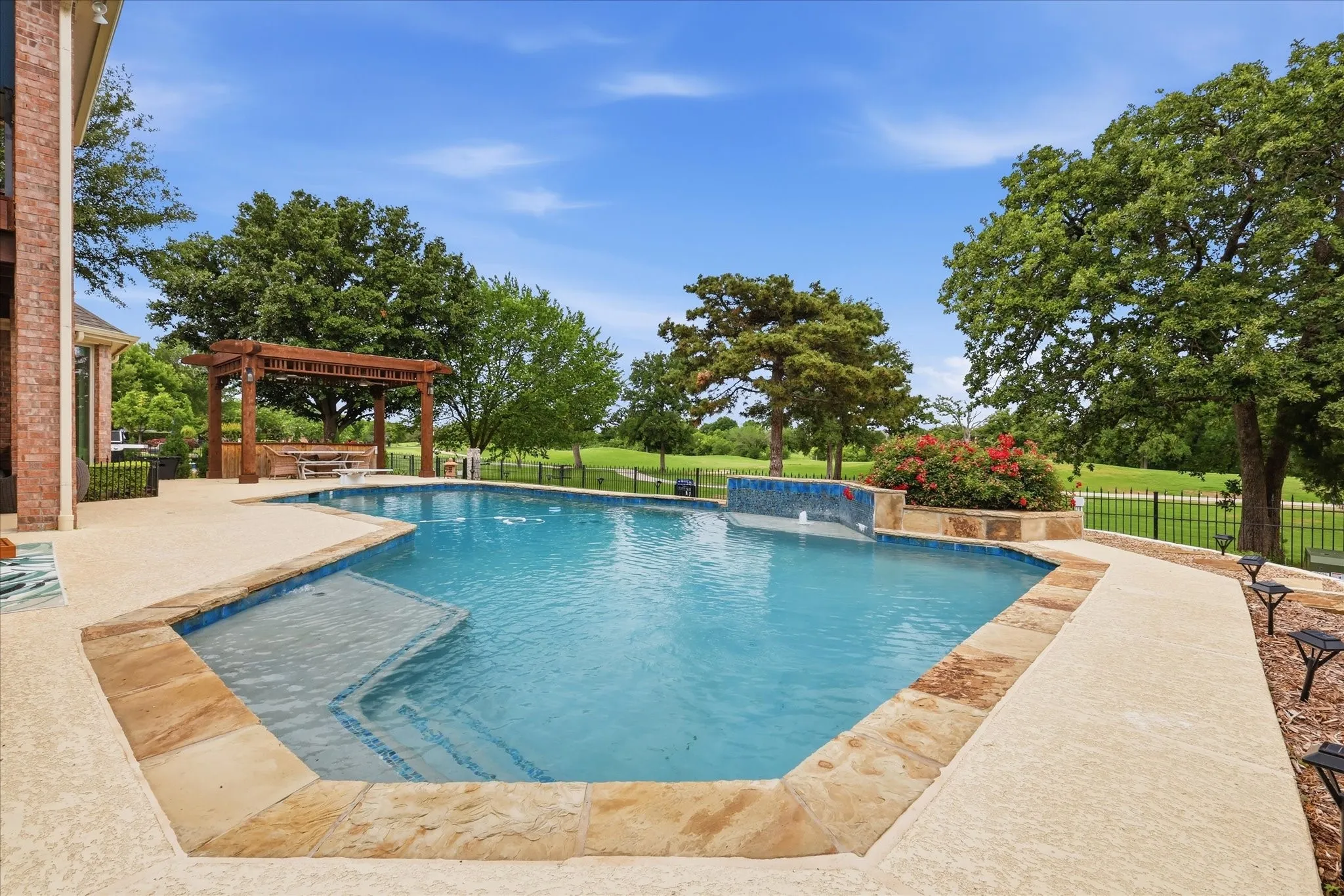 Outdoor oasis featuring a custom-shaped pool with integrated steps, a natural stone coping, and a tiled water feature