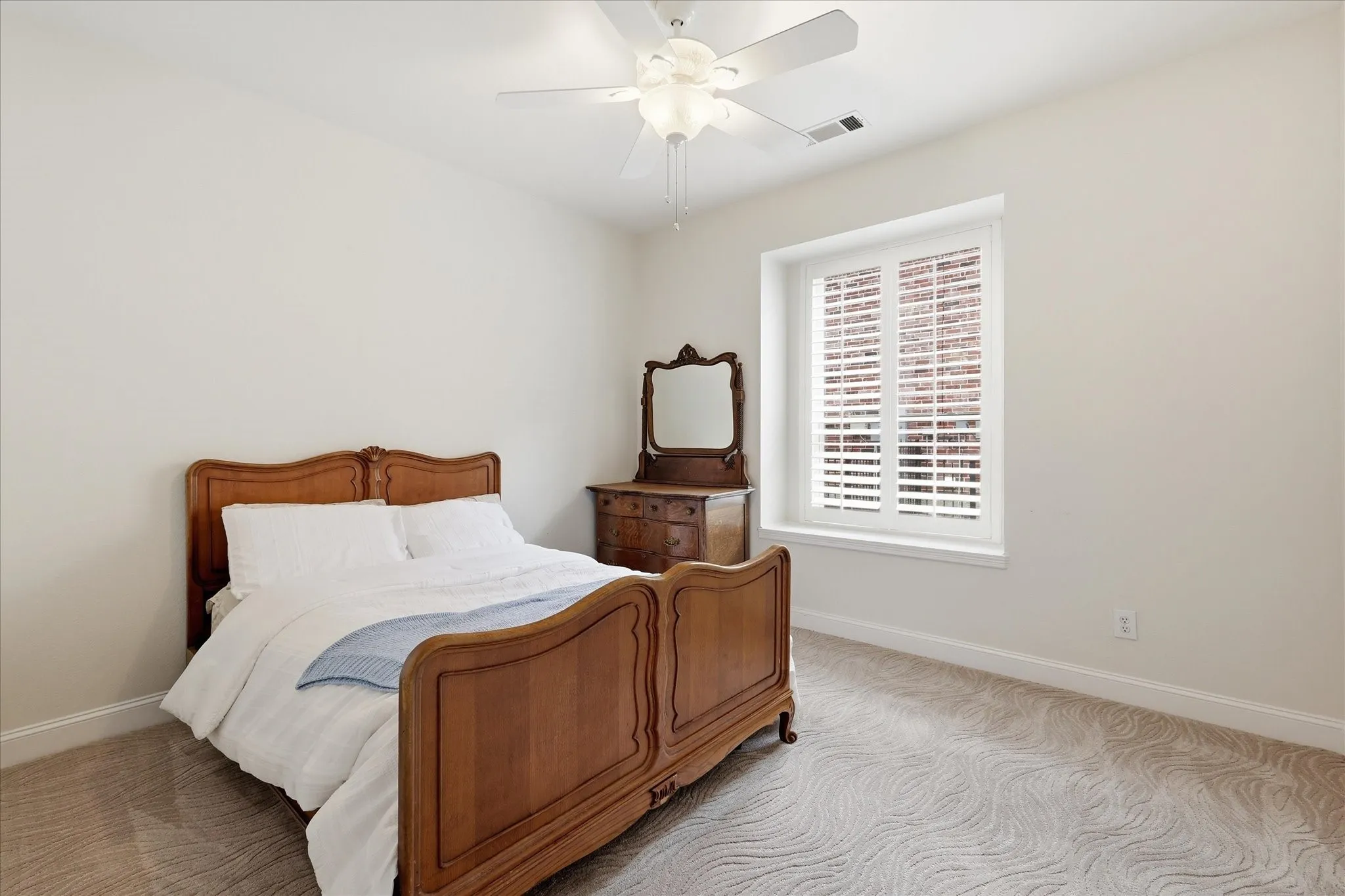 Room featuring a window with white louvered shutters, light-toned walls, and patterned carpeting