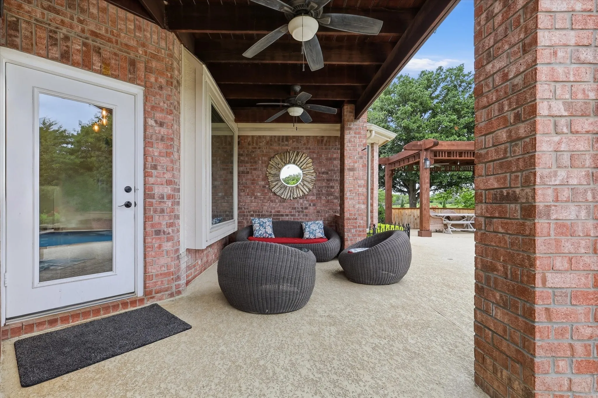 Covered patio featuring brick construction, a stamped concrete surface, ceiling fans, and a distant pergola