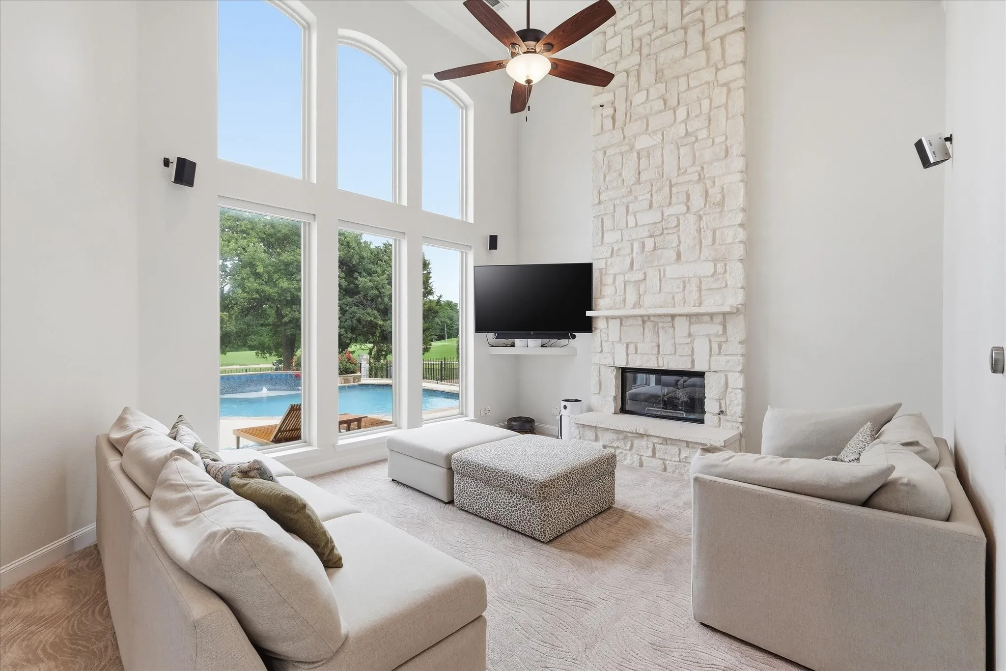 Two-story living area featuring a stone fireplace, arched window accents, and a ceiling fan