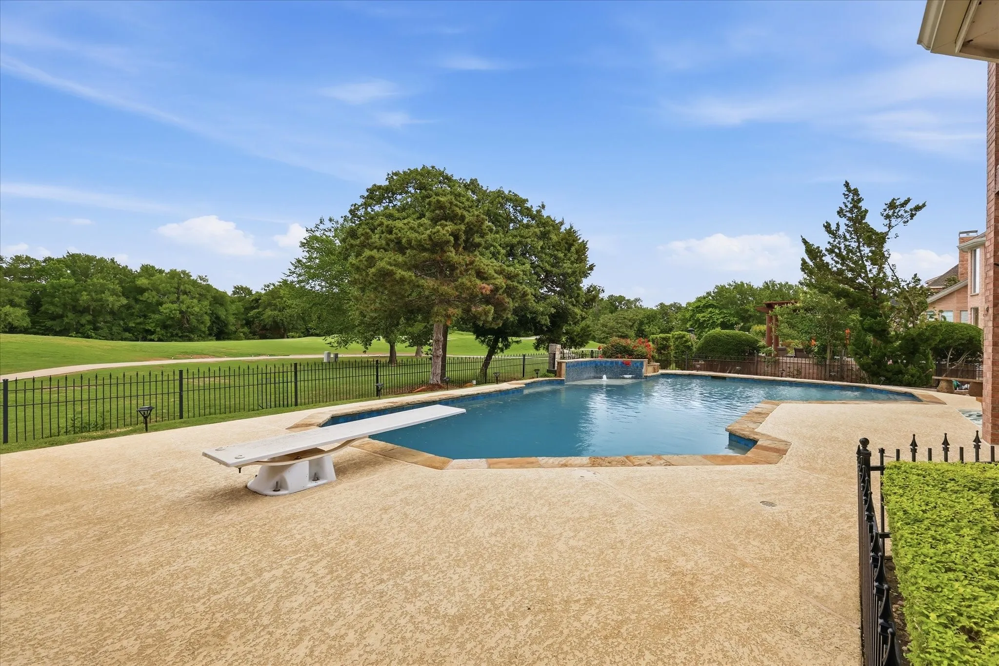 Custom-shaped swimming pool with an integrated diving board, surrounded by a textured concrete patio