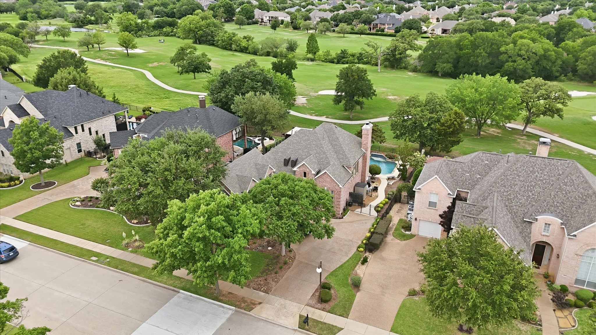 Aerial perspective showcasing a property with a brick exterior, an in-ground swimming pool, and an expansive paved driveway