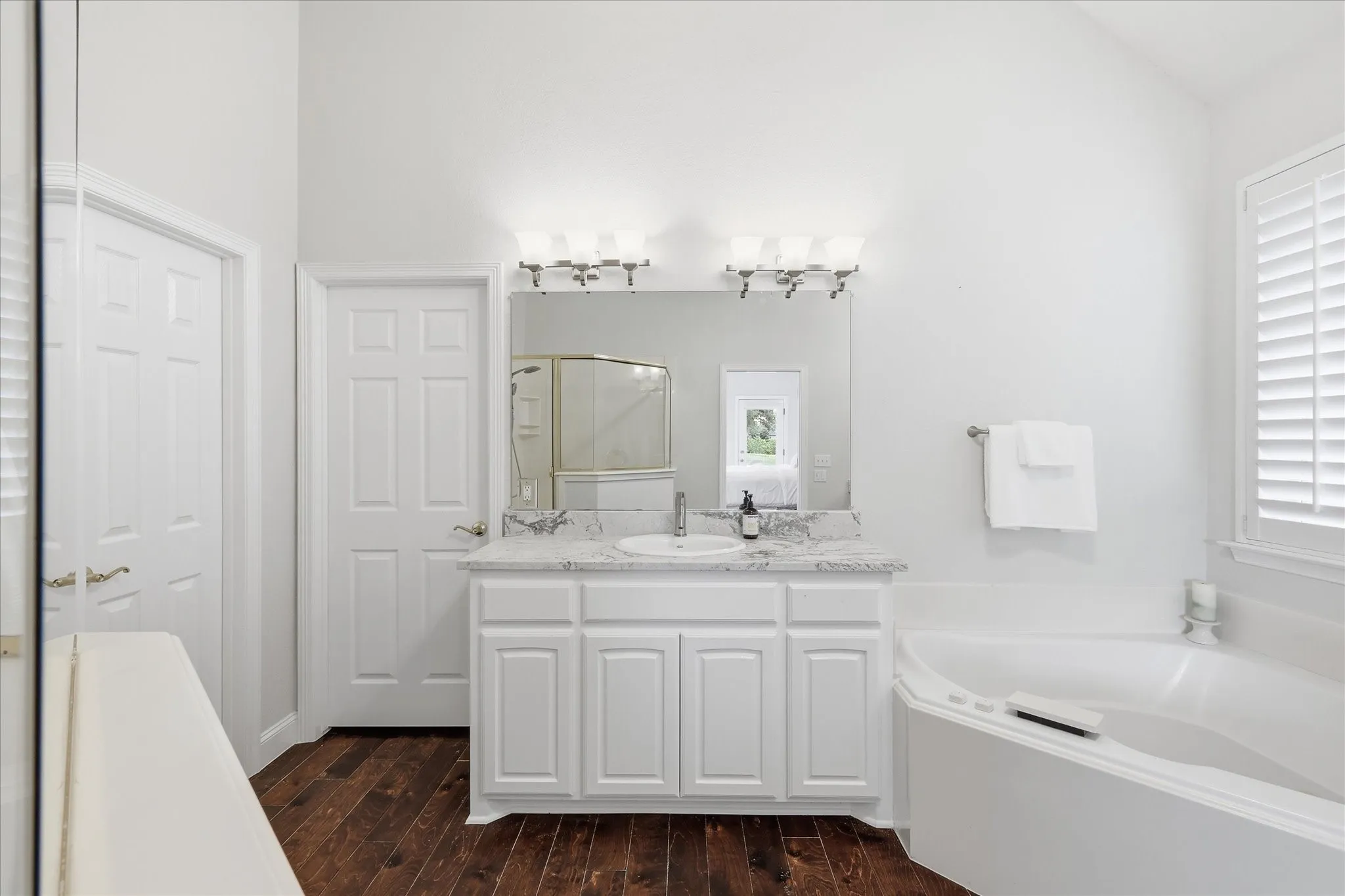 White cabinetry with a polished stone countertop, a drop-in sink, and a framed mirror with vanity lighting
