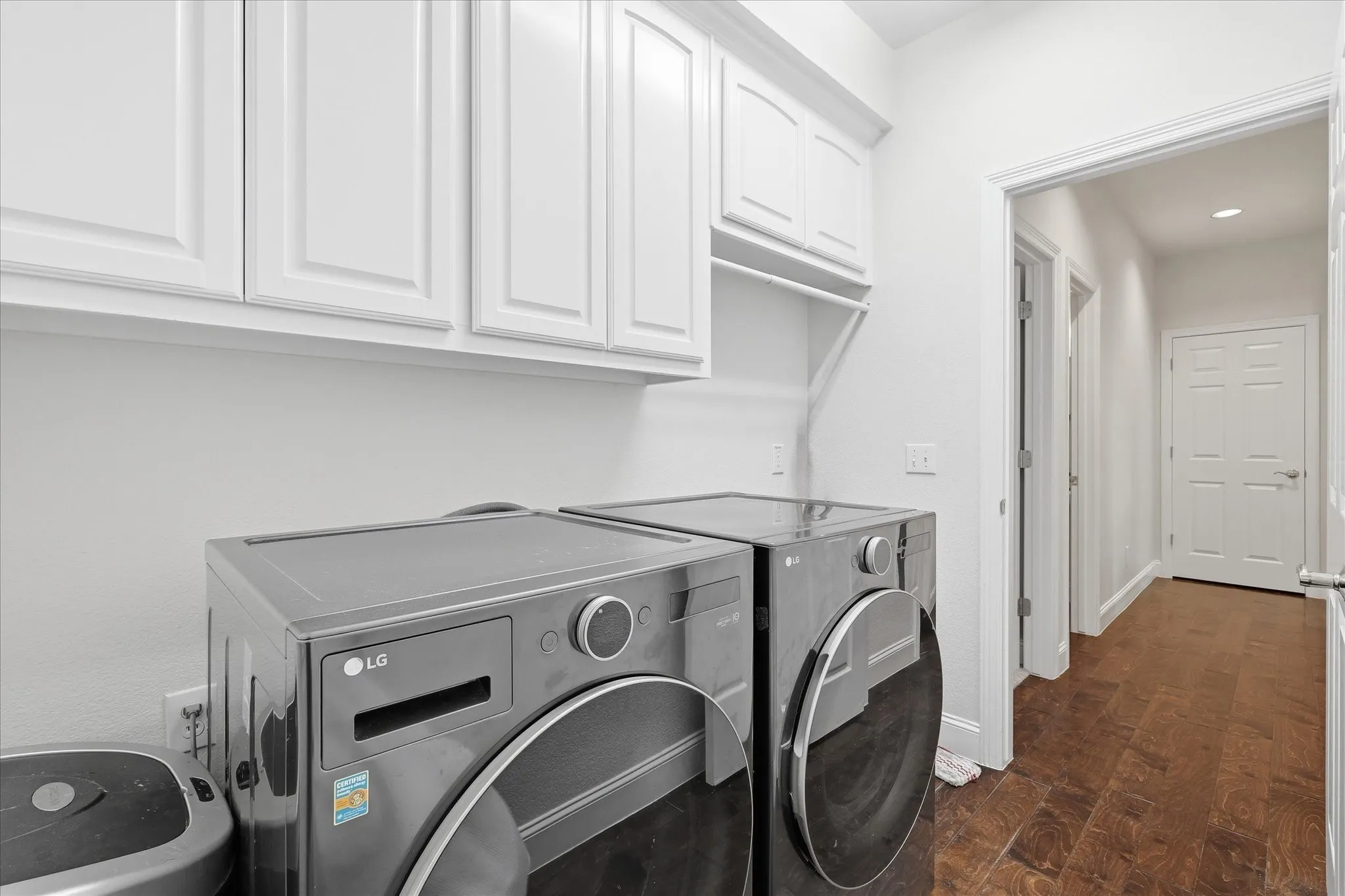 Laundry space featuring white shaker-style cabinetry, wood-finish flooring, and white trim
