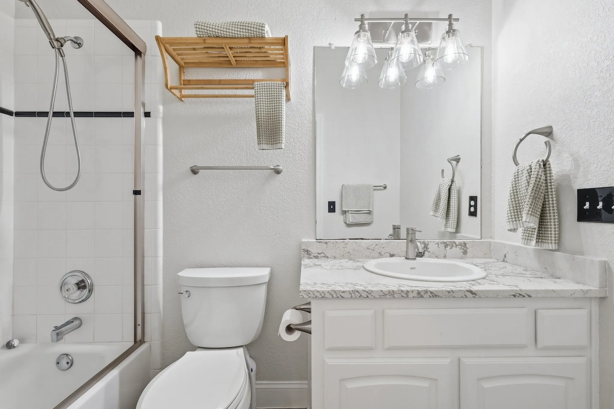 Bathroom featuring a vanity with white cabinetry, a light fixture, a mirror, and a shower-tub combination with a glass enclosure
