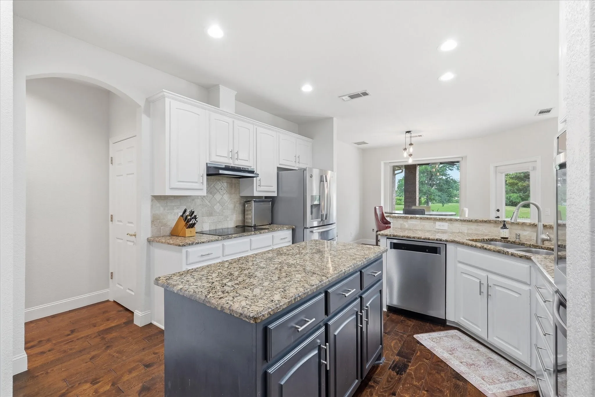 Kitchen featuring a central island with a granite countertop, white cabinetry, stainless steel appliances, and wood-finish flooring