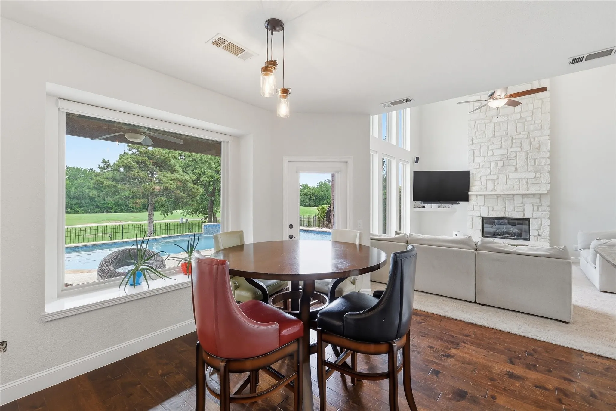 Open concept living area with dark wood-finish flooring, a stone fireplace, and a large window overlooking a swimming pool