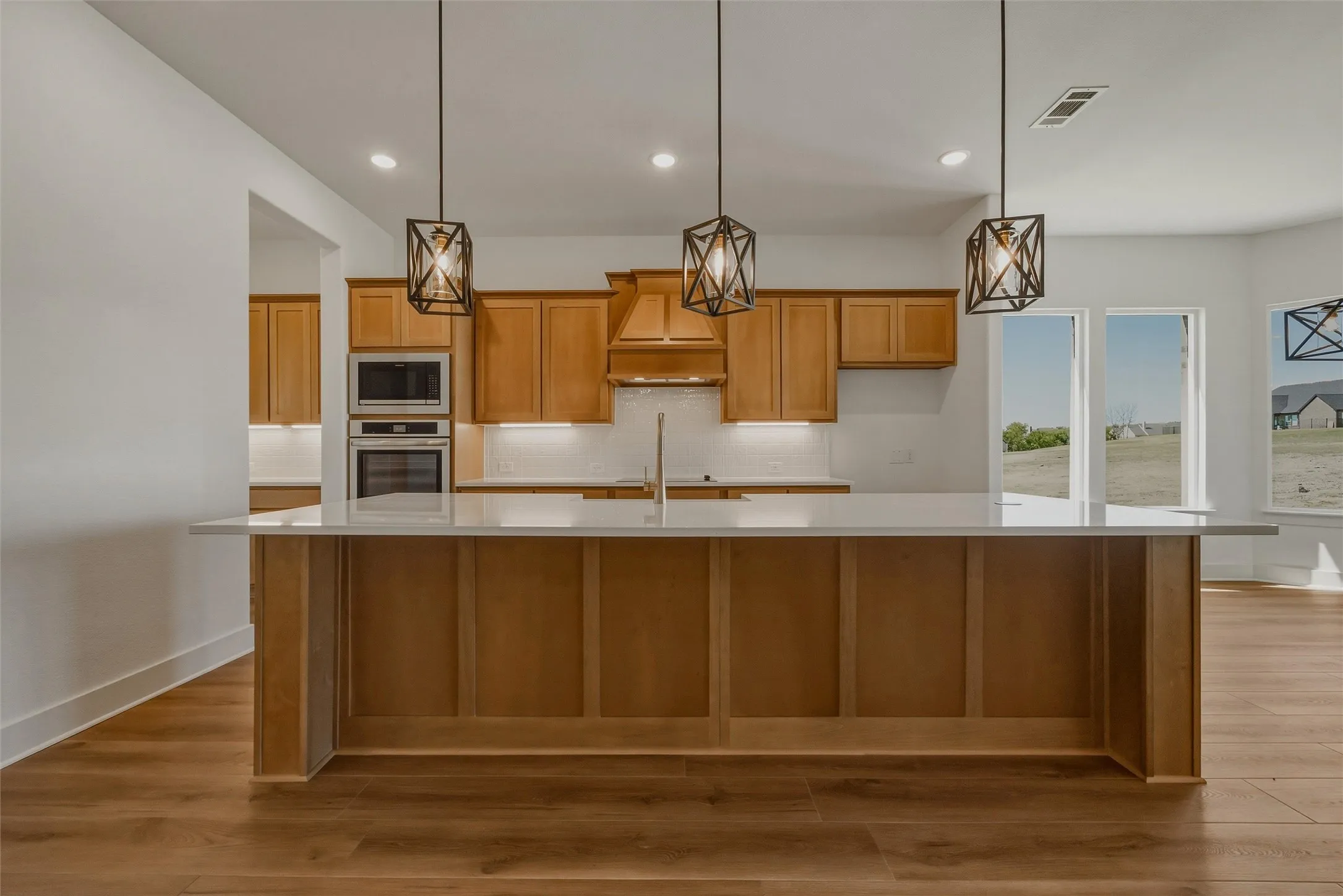 Open-concept kitchen with a large island, wood-finish cabinetry, stainless steel appliances, and pendant lighting