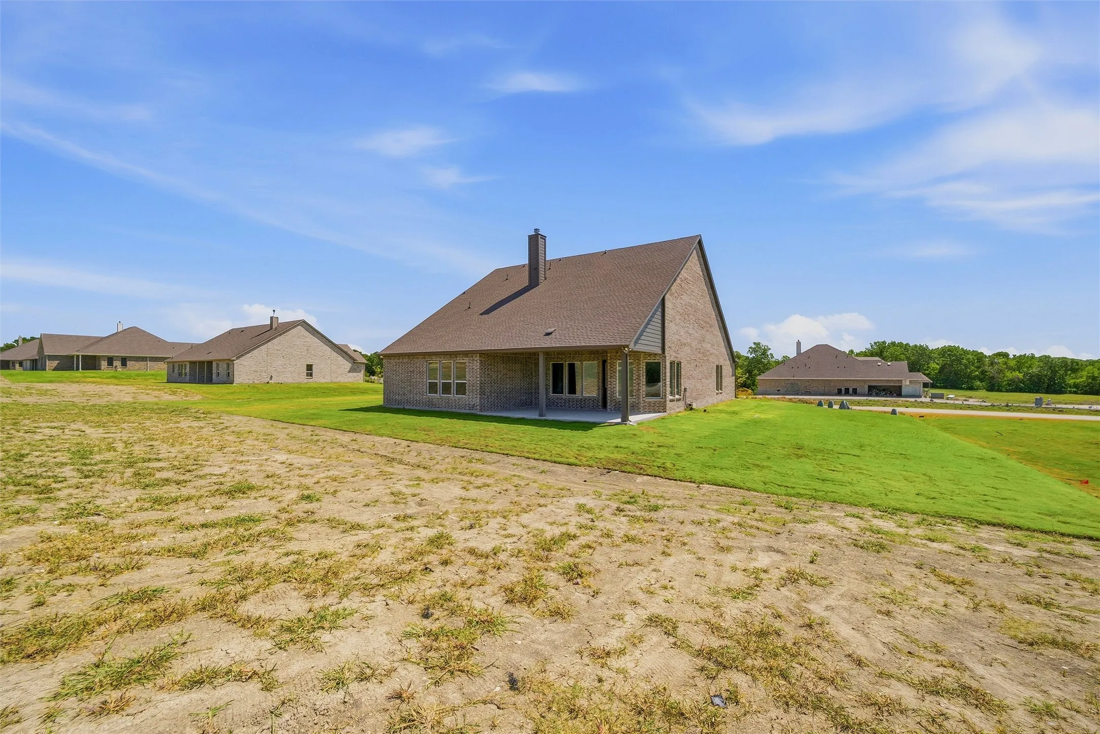 Brick exterior, covered patio, multiple windows, sloped lawn, shingle roof