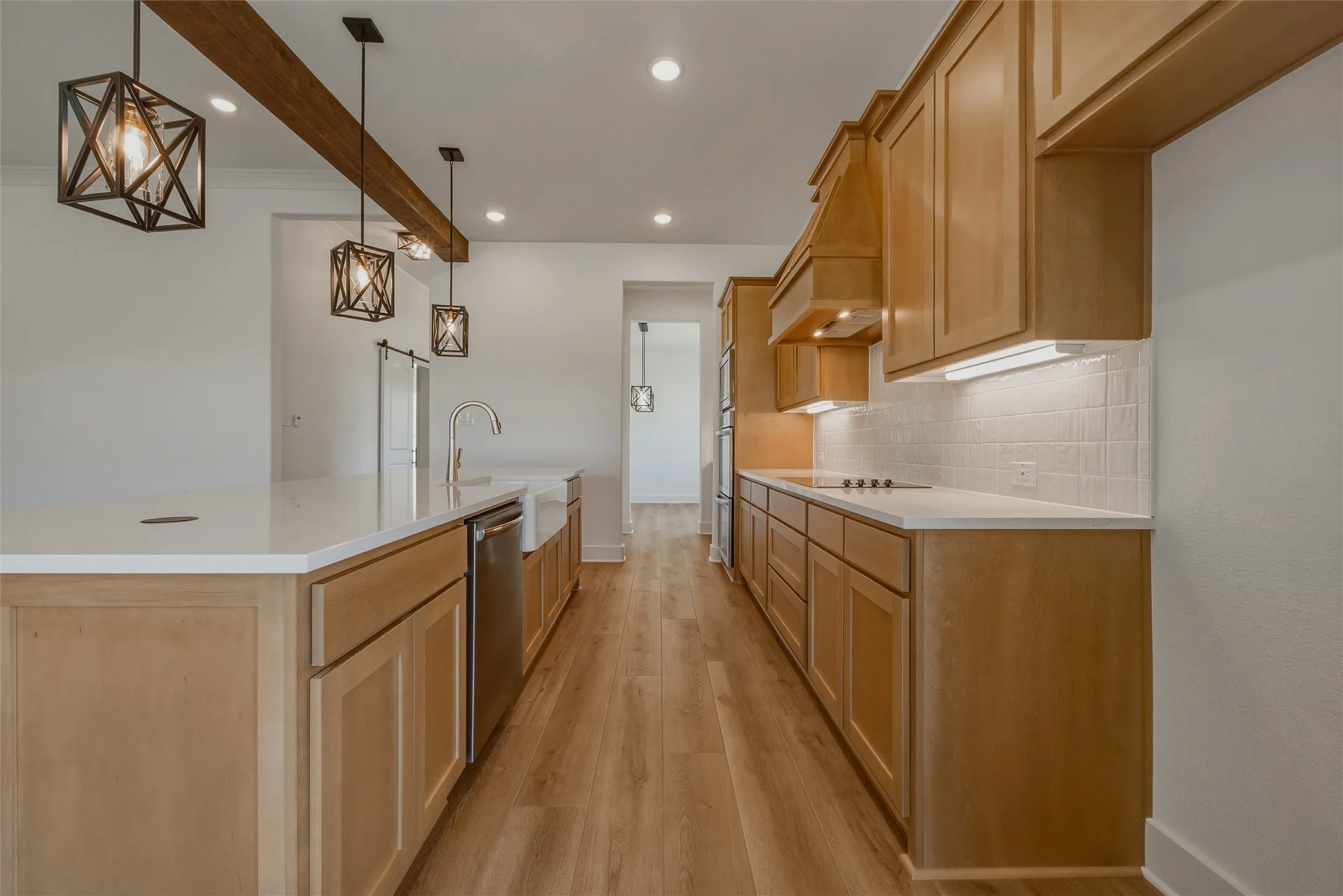 Wood-finish flooring, white countertops, light wood cabinetry, stainless steel appliances, and a farmhouse sink