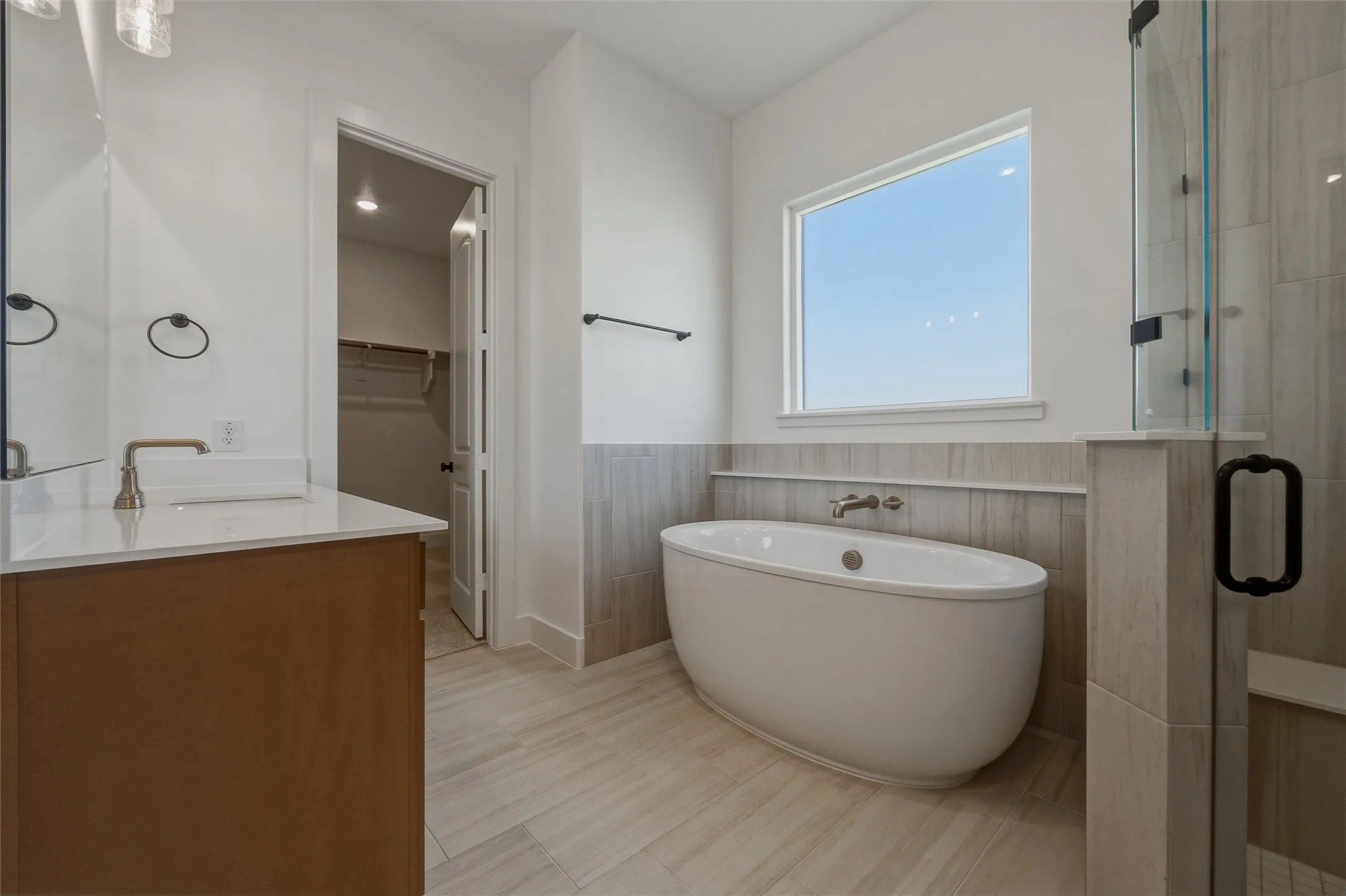 Freestanding soaking tub with wall-mounted faucet, glass-enclosed shower with tile surround, wood-finish vanity with countertop, and rectangular vessel sink