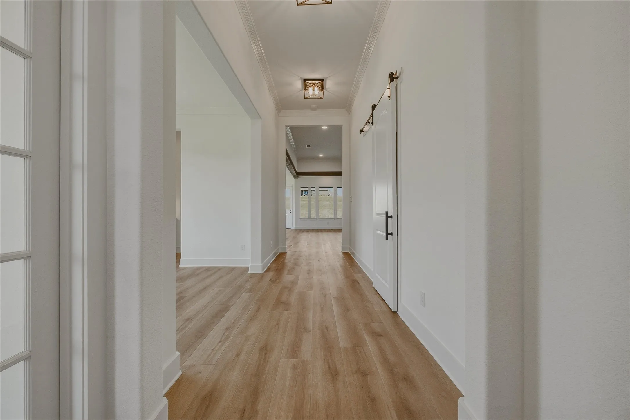 Hallway featuring wood-finish flooring, recessed lighting, crown molding, and a white barn door with black hardware