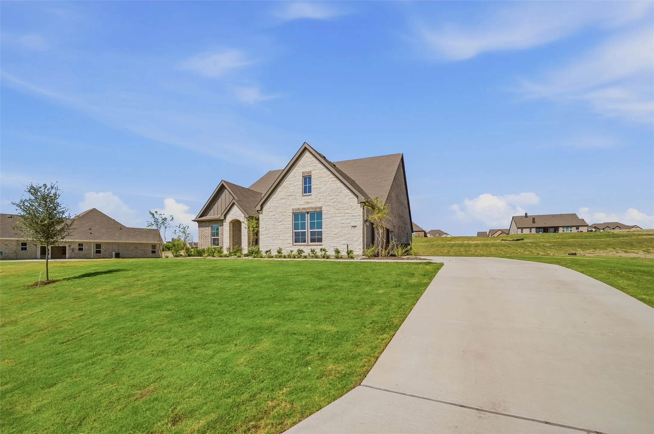 Stone and brick facade, gabled roofline, concrete driveway, and established landscaping