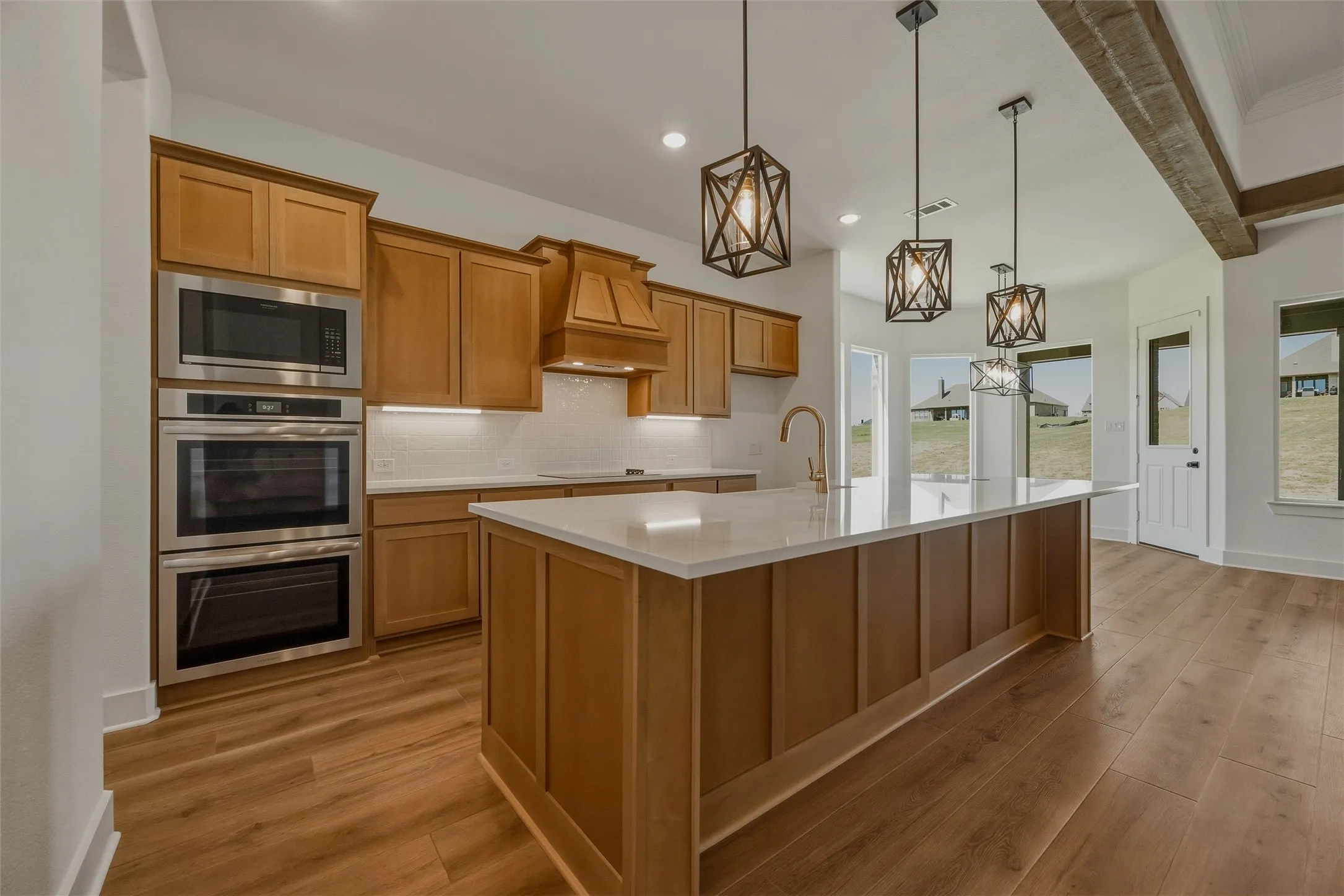 Kitchen featuring wood-finish flooring, built-in double ovens, a large center island with pendant lighting, and exposed ceiling beams