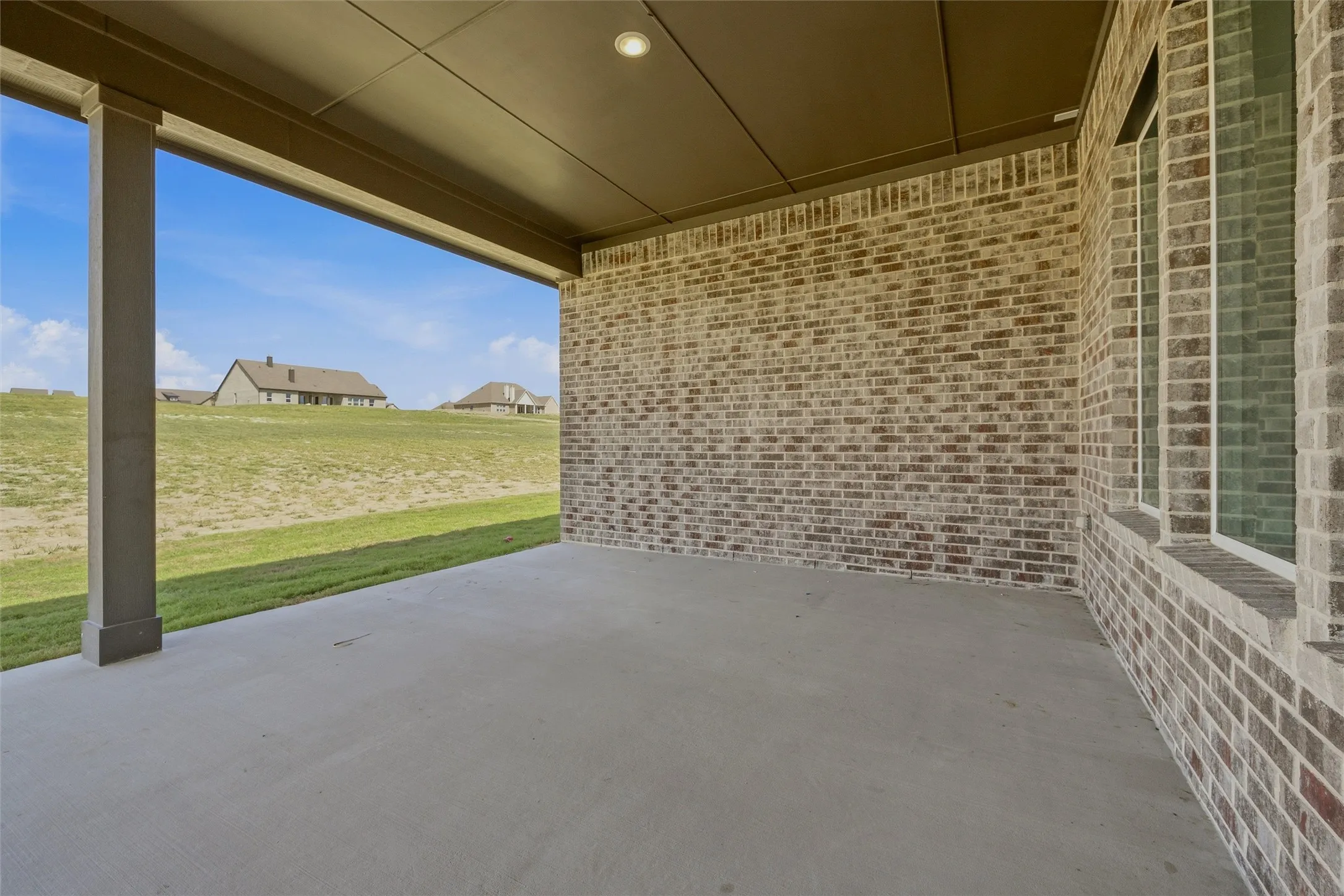 Covered patio with a concrete surface, brick exterior wall, recessed lighting, and multiple windows
