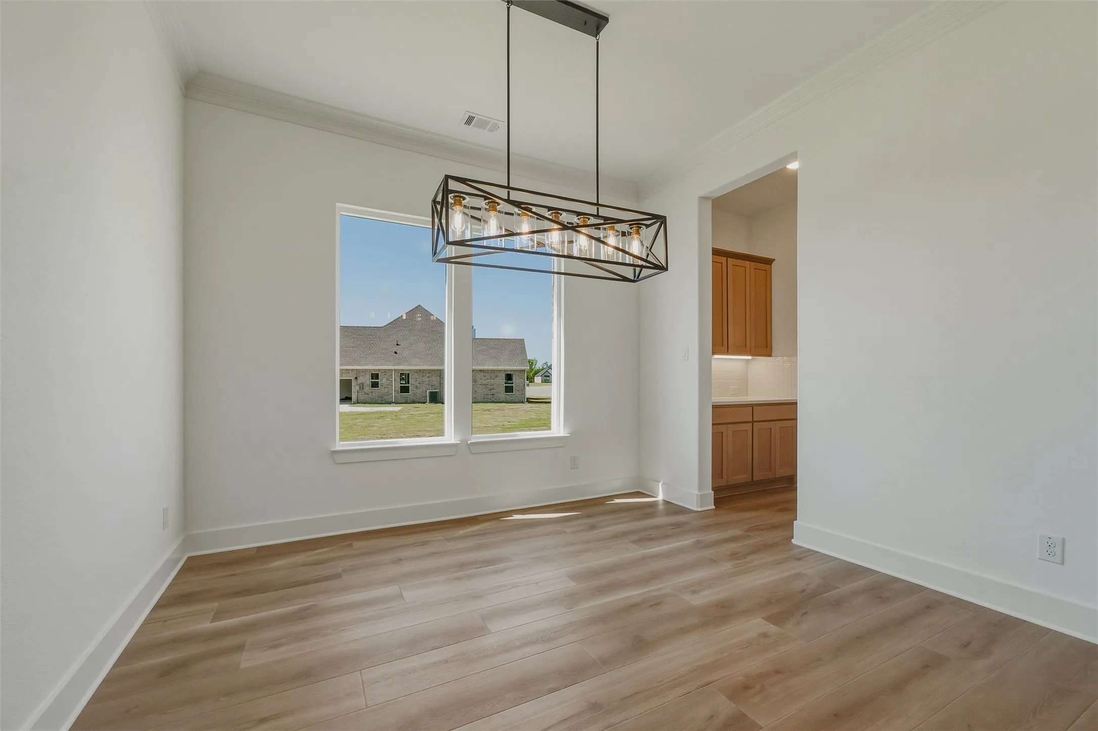 Wood-finish flooring with white baseboards, crown molding, and a modern rectangular chandelier