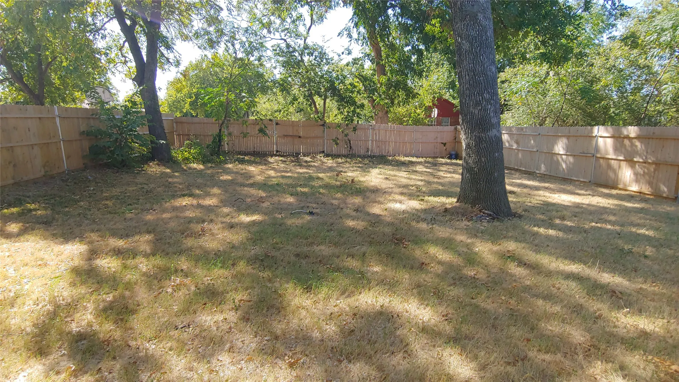 Notice this spacious backyard with wood fence and mature trees.