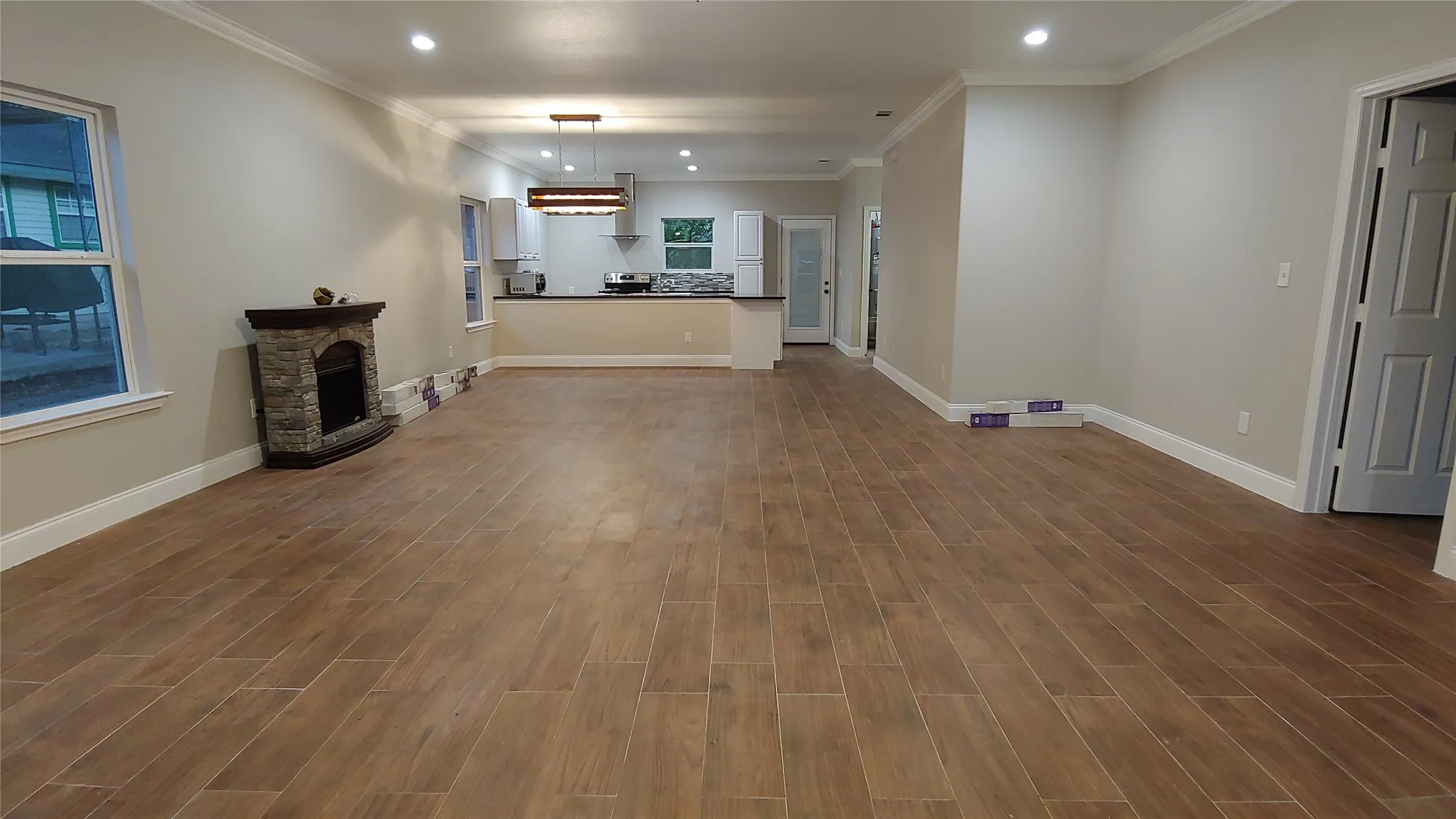 Spacious open-concept interior featuring wood-finish tile flooring, recessed lighting, and a stone-clad fireplace