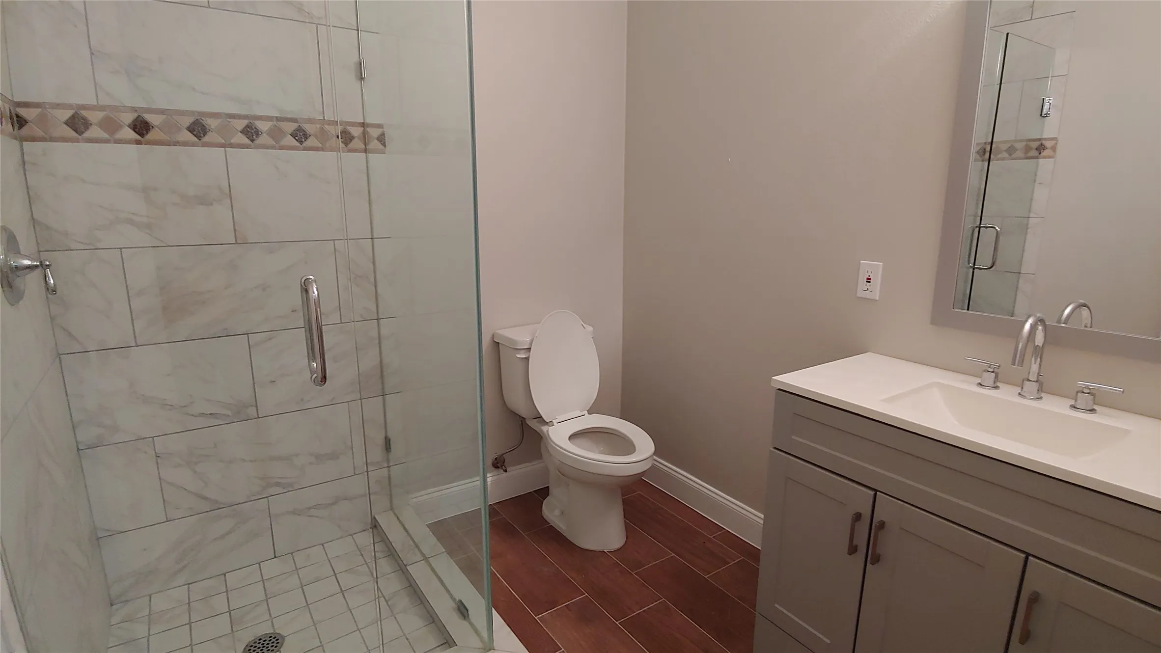 Glass-enclosed shower with white tiled walls and decorative accent band