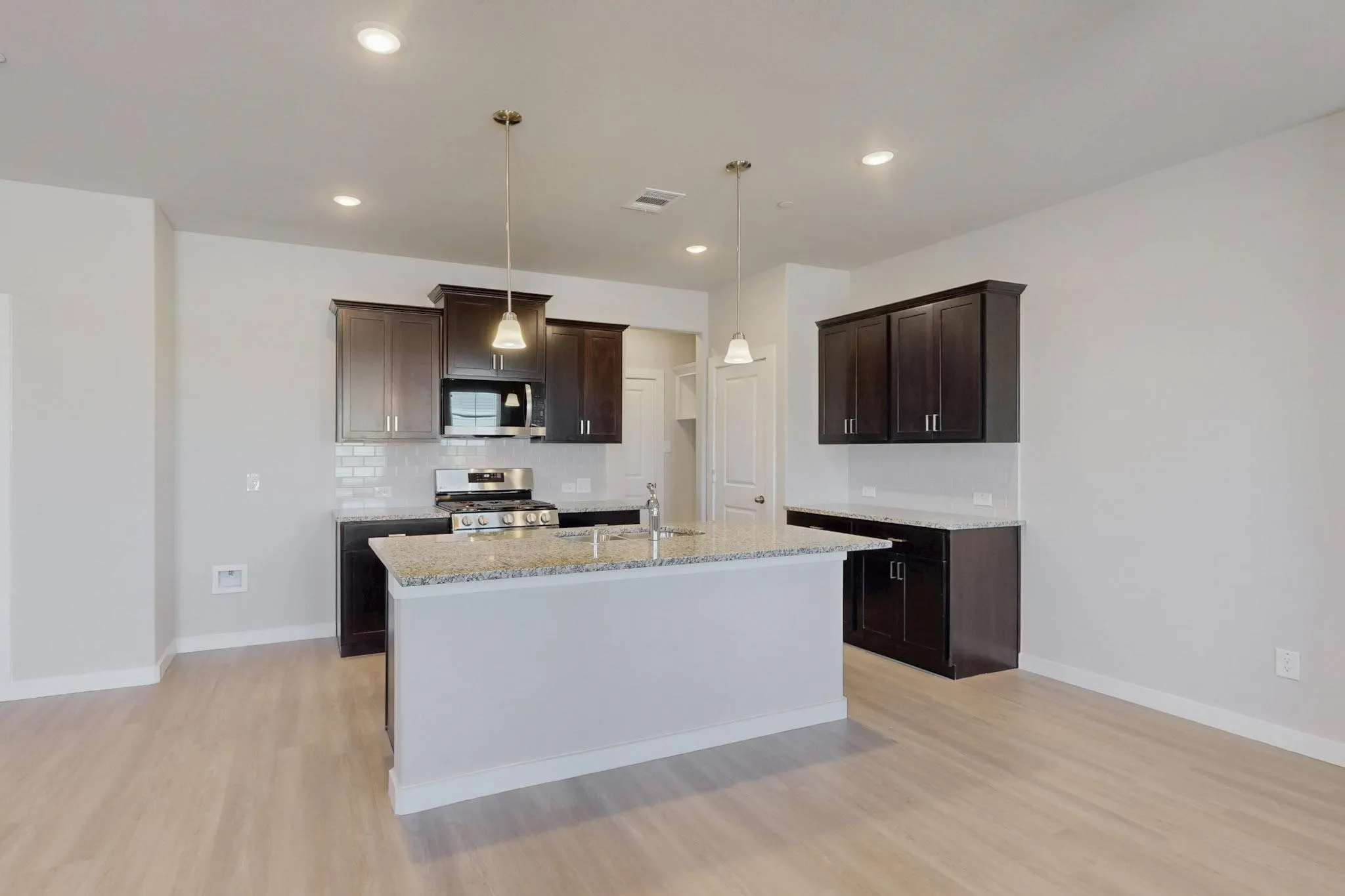 Kitchen with dark brown cabinets, stainless steel appliances, light wood-style floors, light stone countertops, and a kitchen island with sink