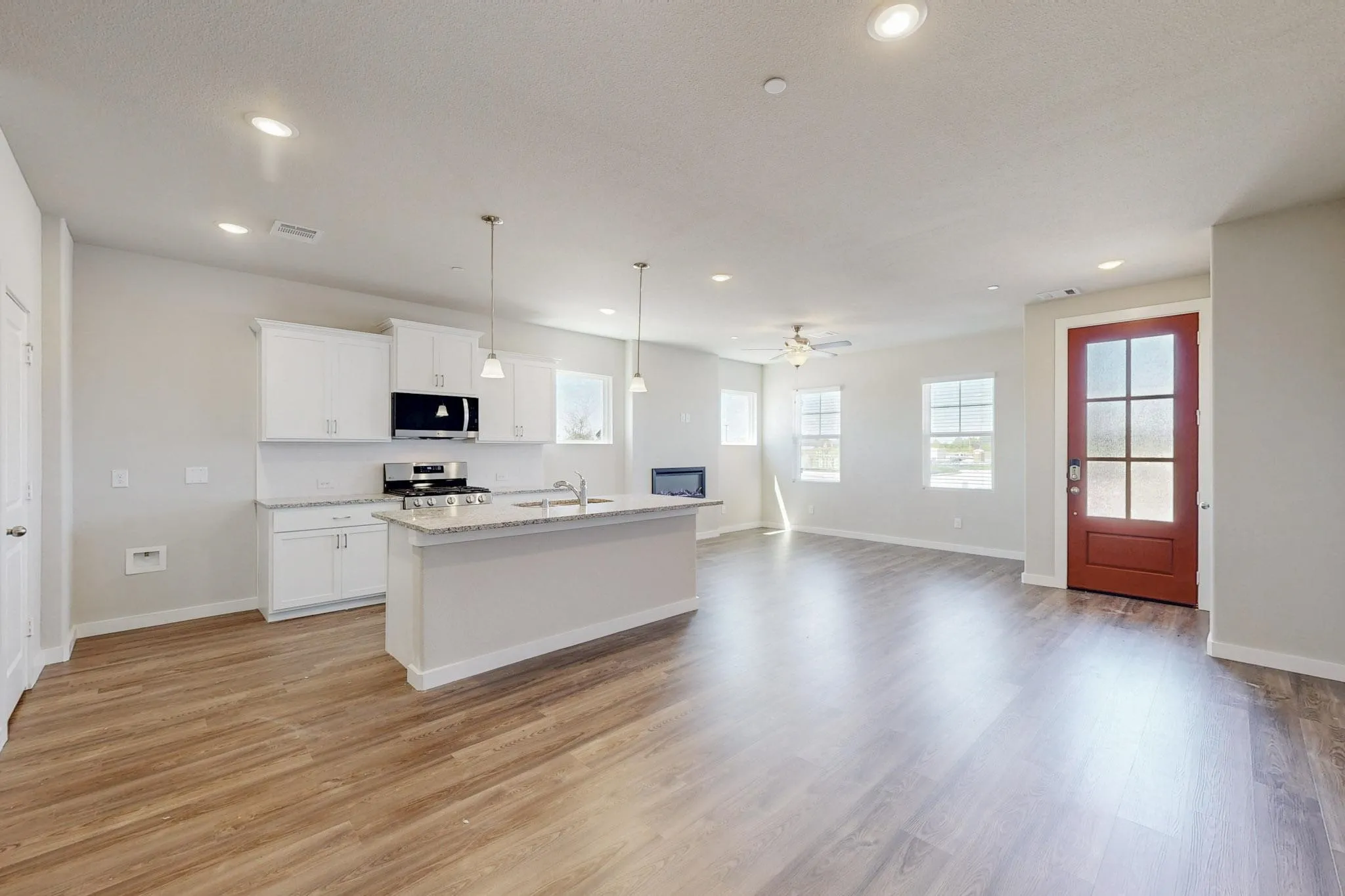 Kitchen with pendant lighting, an island with sink, open floor plan, white cabinetry, and appliances with stainless steel finishes