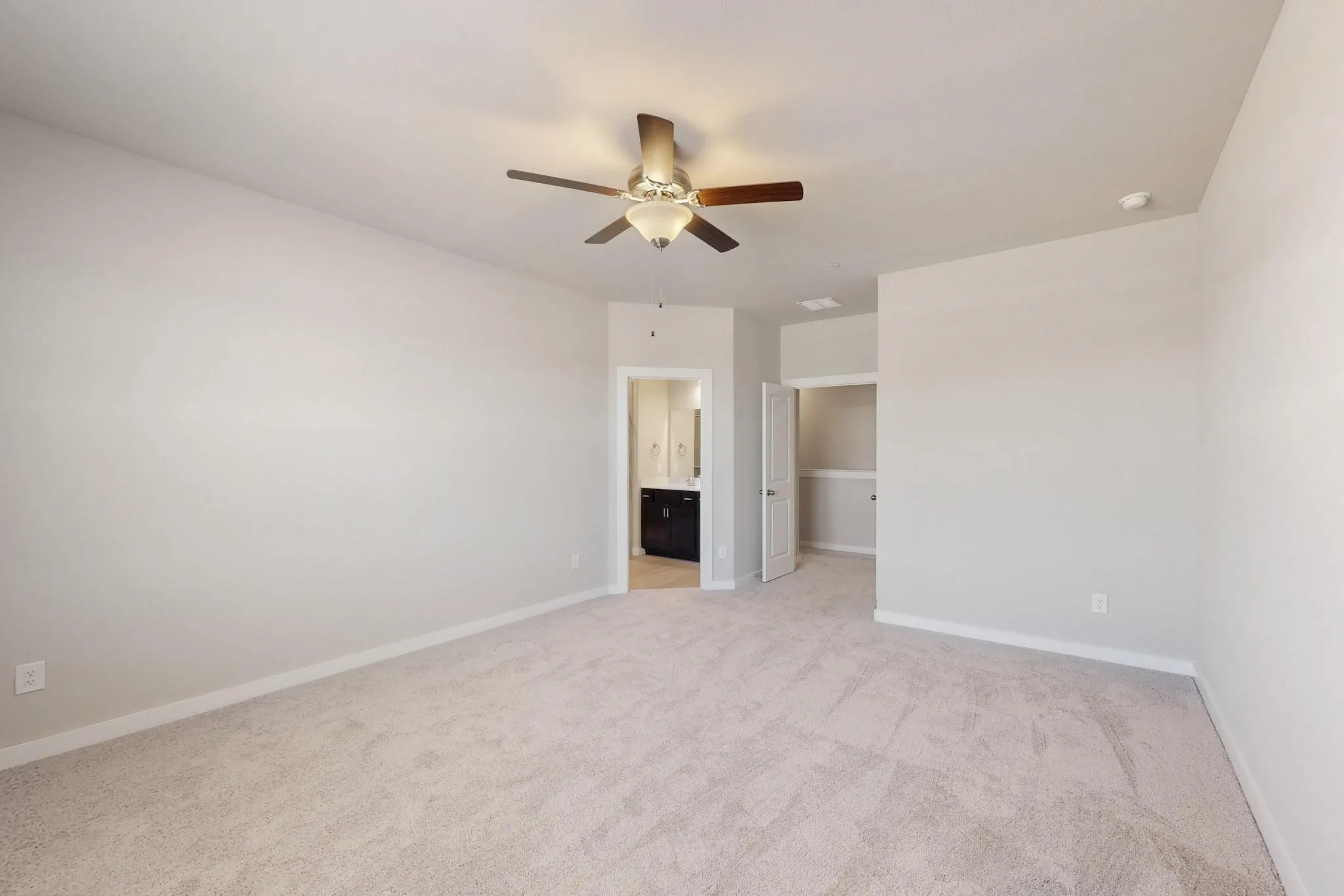 Unfurnished bedroom featuring a spacious closet, light carpet, a ceiling fan, and ensuite bath