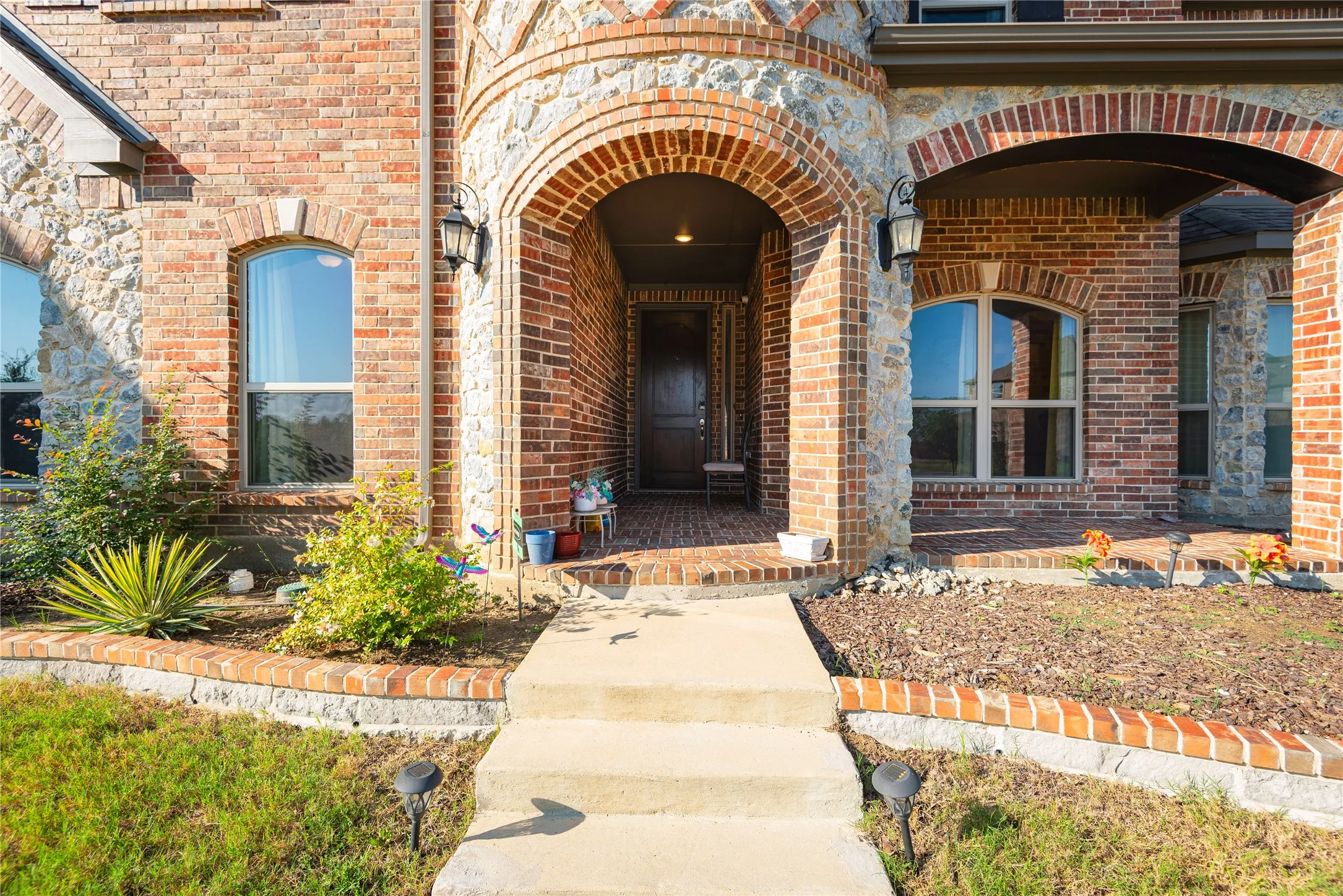 Brick and stone exterior featuring an arched entryway, covered porch, and arched windows