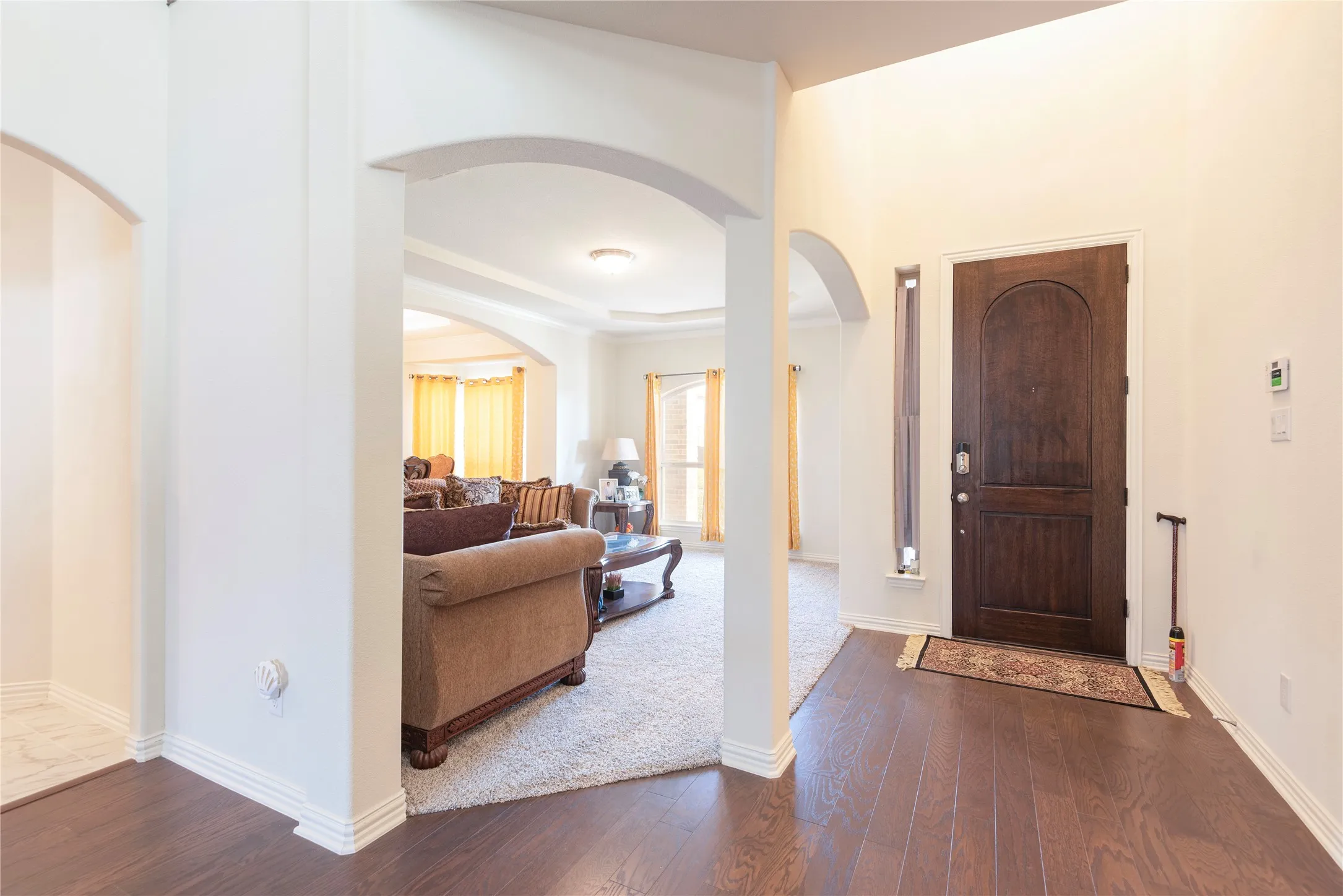Entryway featuring a dark wood-finish door with an arched top panel, an adjacent vertical window, and wood-finish flooring