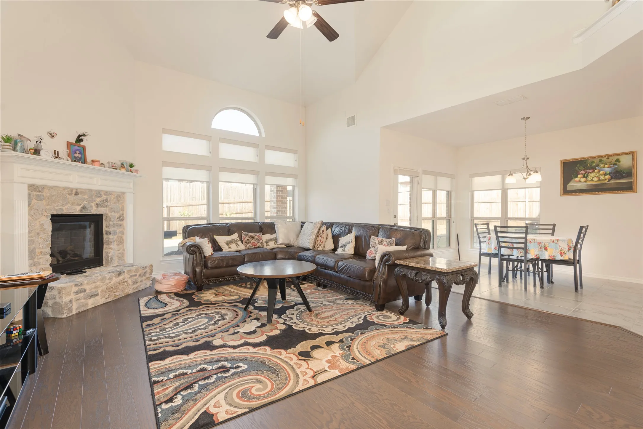 Spacious living area featuring a stone fireplace with a white mantel, vaulted ceilings, and wood-finish flooring