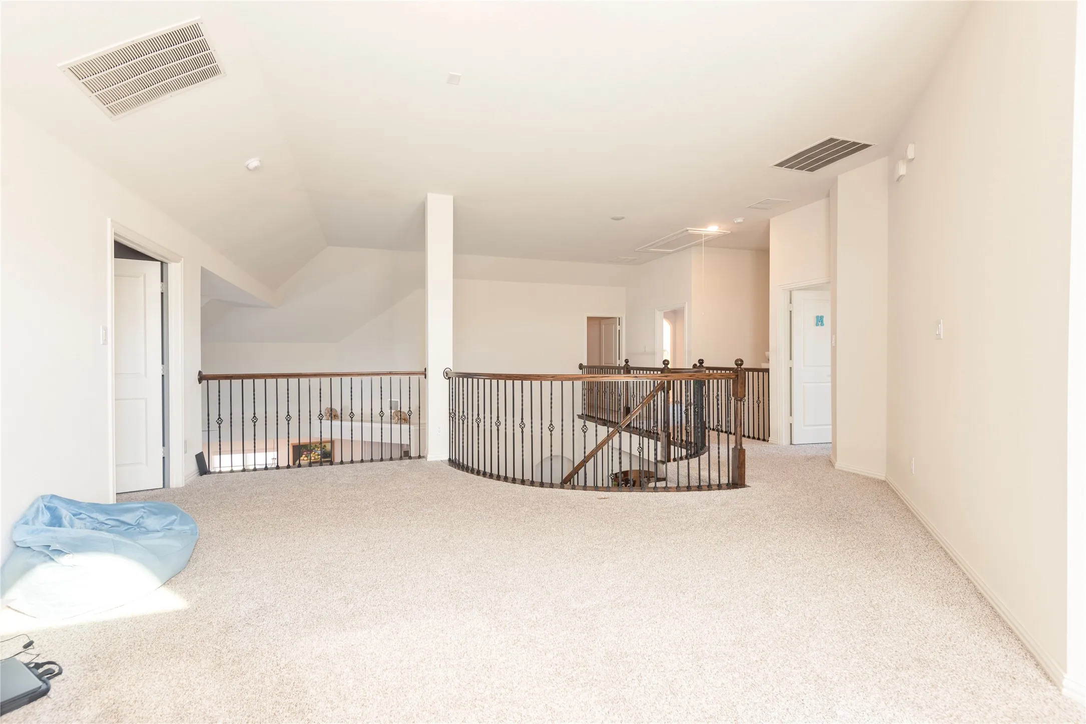 Expansive carpeted loft area with iron and wood railings, vaulted ceilings, and recessed lighting