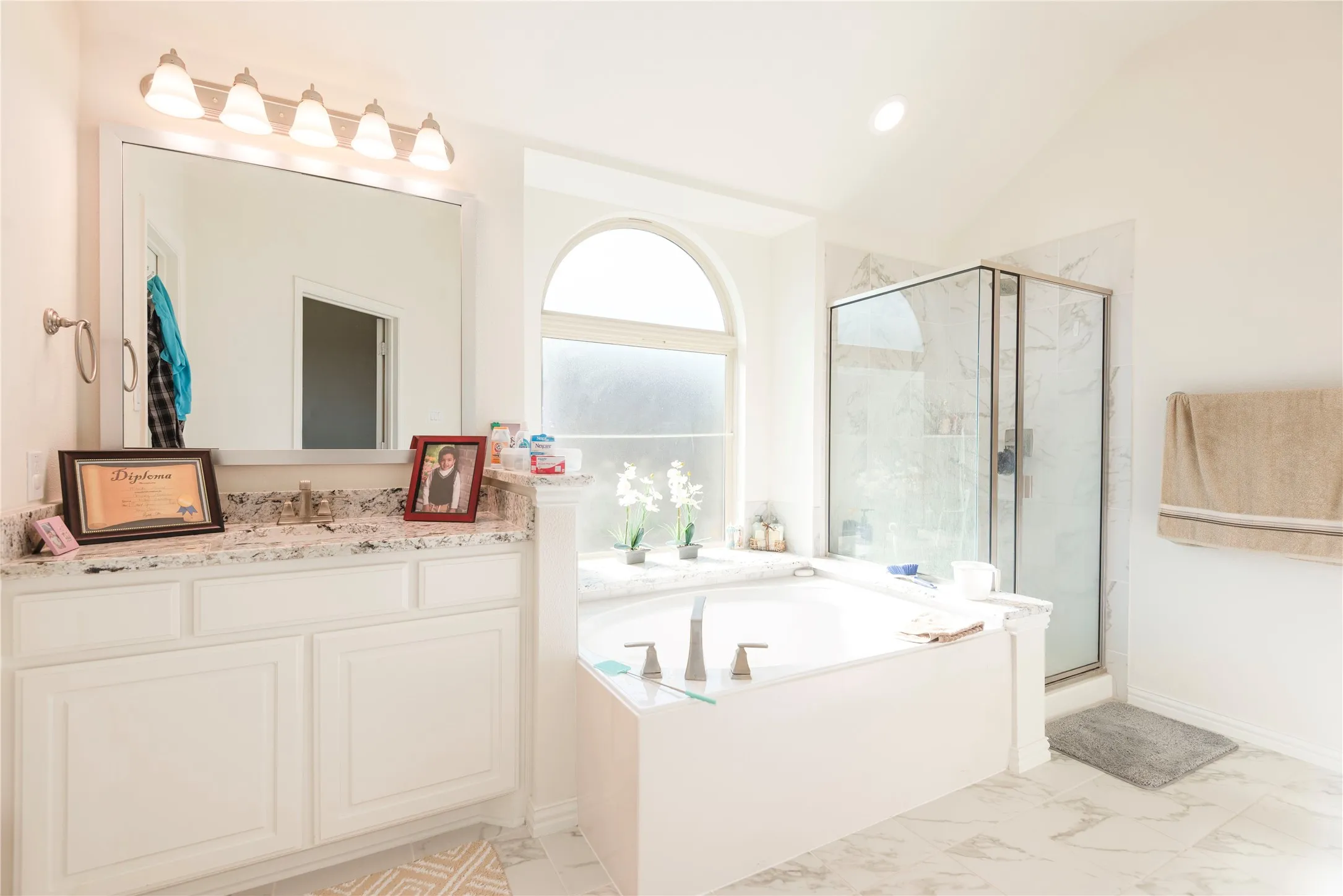 Bathroom featuring a built-in tub, separate glass-enclosed shower, arched window, and a vanity with a stone countertop