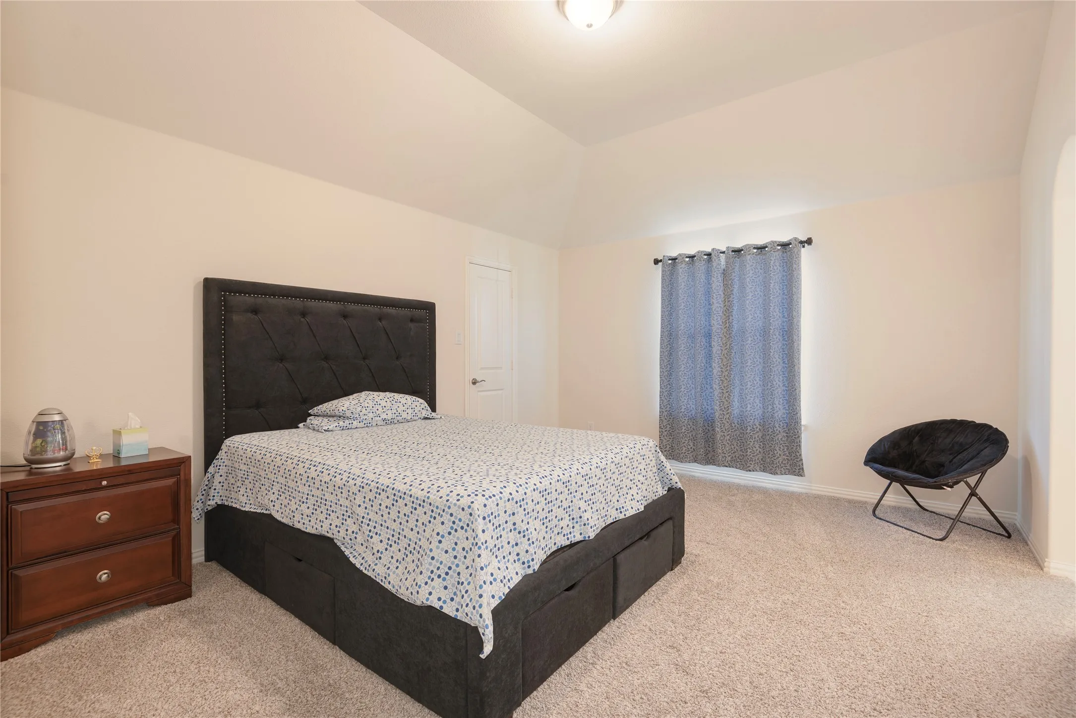 Carpeted room featuring a vaulted ceiling and a single window with curtain rod