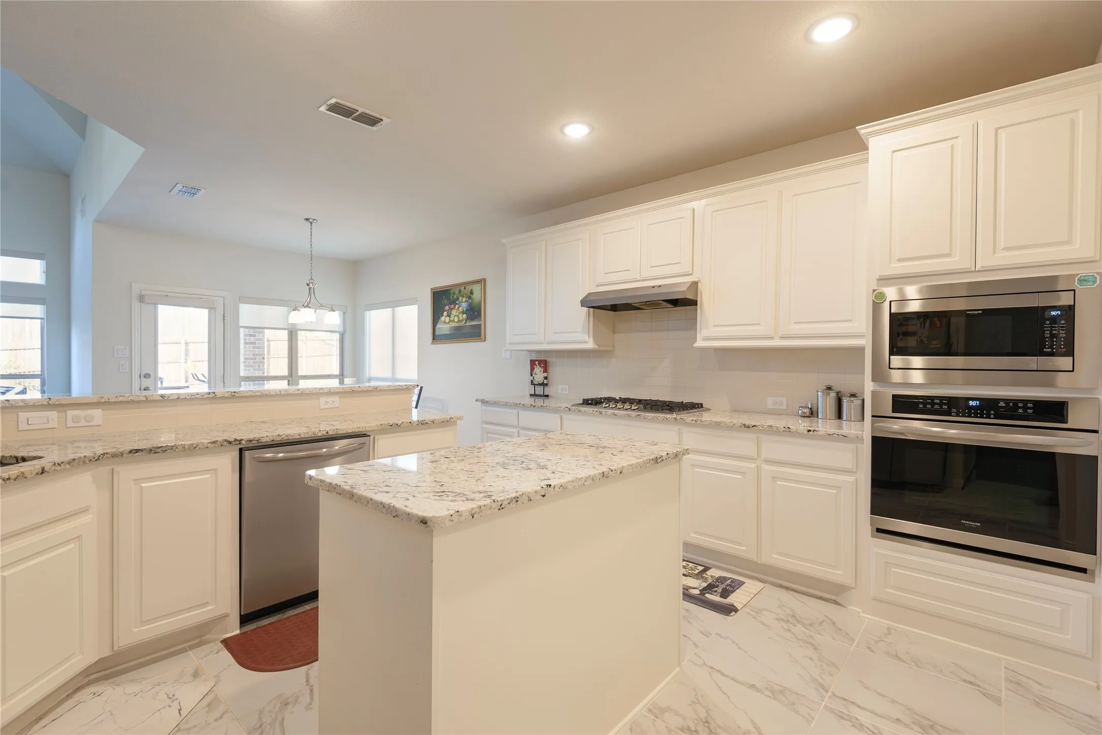 Modern kitchen featuring white shaker cabinetry, speckled stone countertops, stainless steel appliances, a center island, and large format marble-look tile flooring