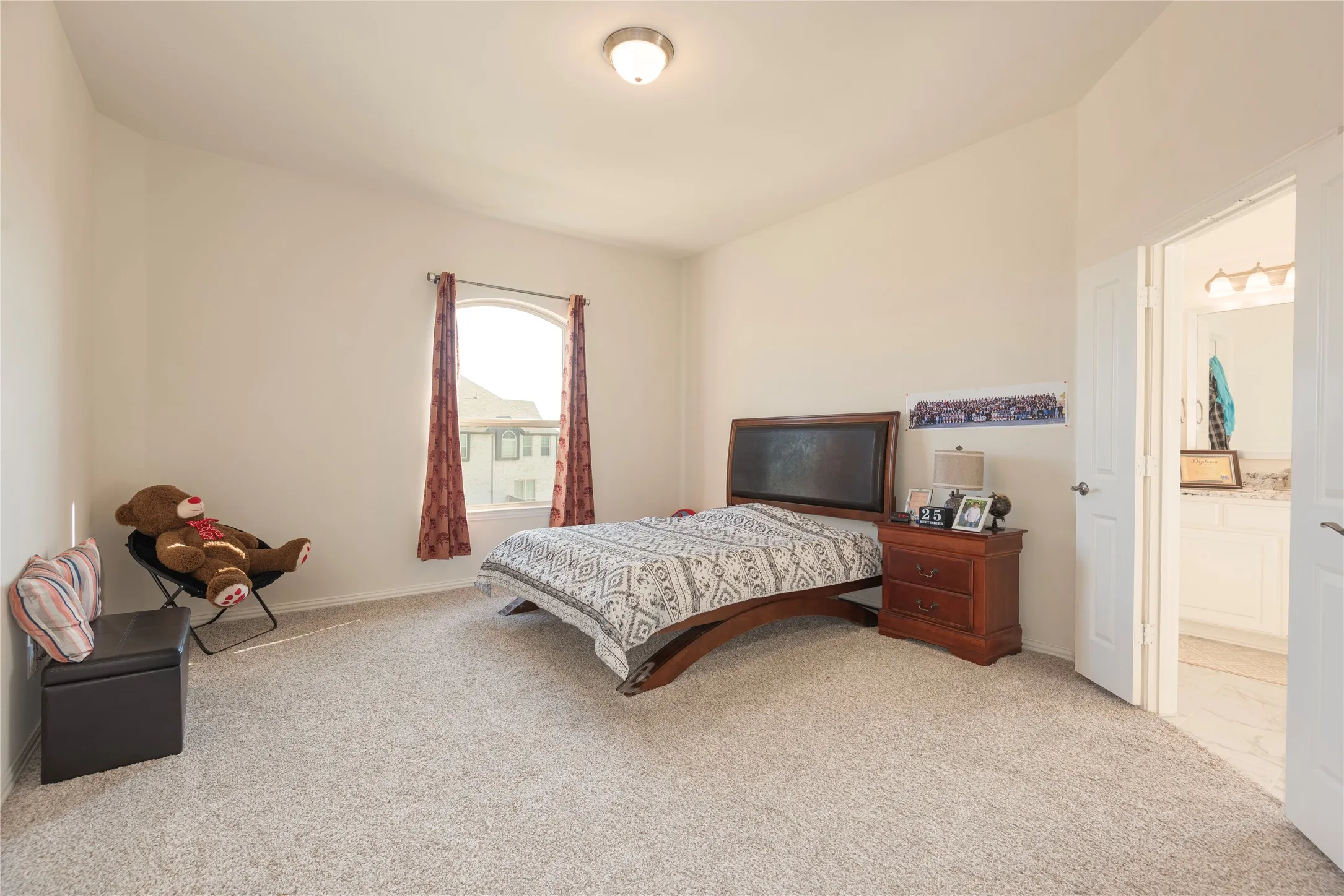 Spacious room featuring vaulted ceilings, a large arched window with drapes, wall-to-wall carpeting, and a visible doorway revealing a bathroom with a white vanity and countertop