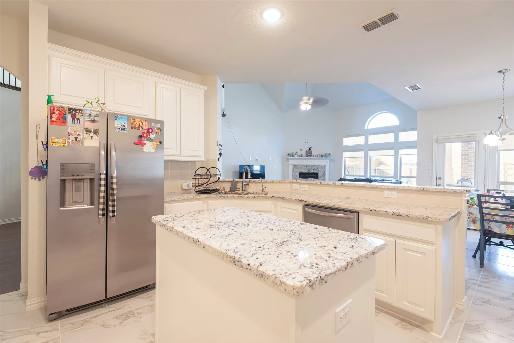 Open-concept kitchen featuring white cabinetry, light granite countertops, a built-in dishwasher, and tile flooring