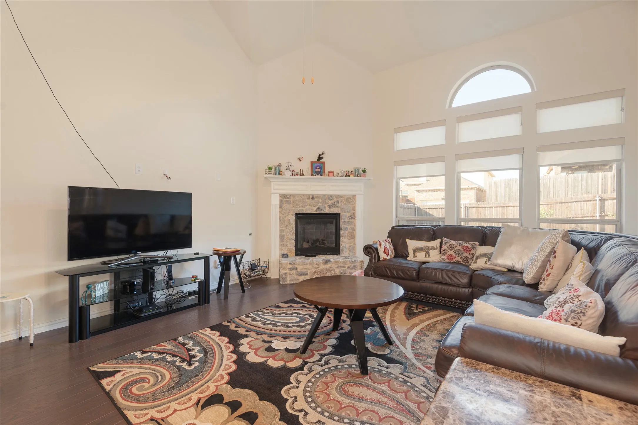 Living area featuring a stone fireplace with a white mantel, wood-finish flooring, and vaulted ceilings