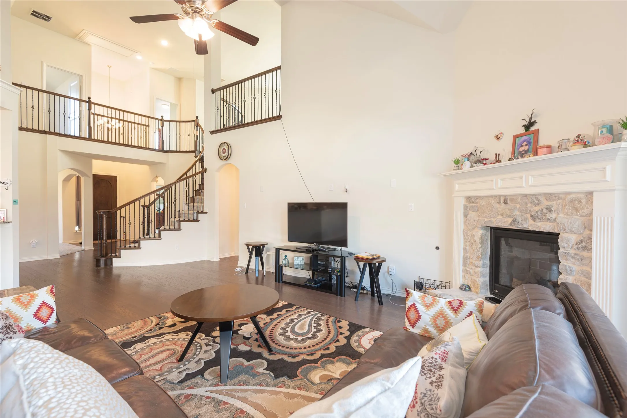 Spacious living area featuring a stone-surround fireplace with a detailed mantel, high vaulted ceilings, and dark wood-finish flooring