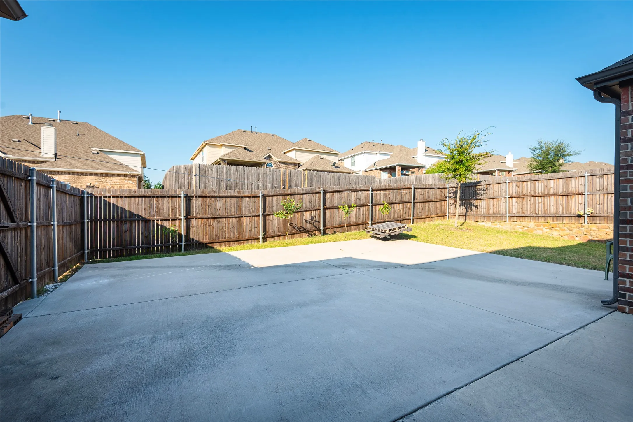 Spacious outdoor area featuring a concrete patio, wood privacy fencing, a section of lawn, and a brick exterior wall